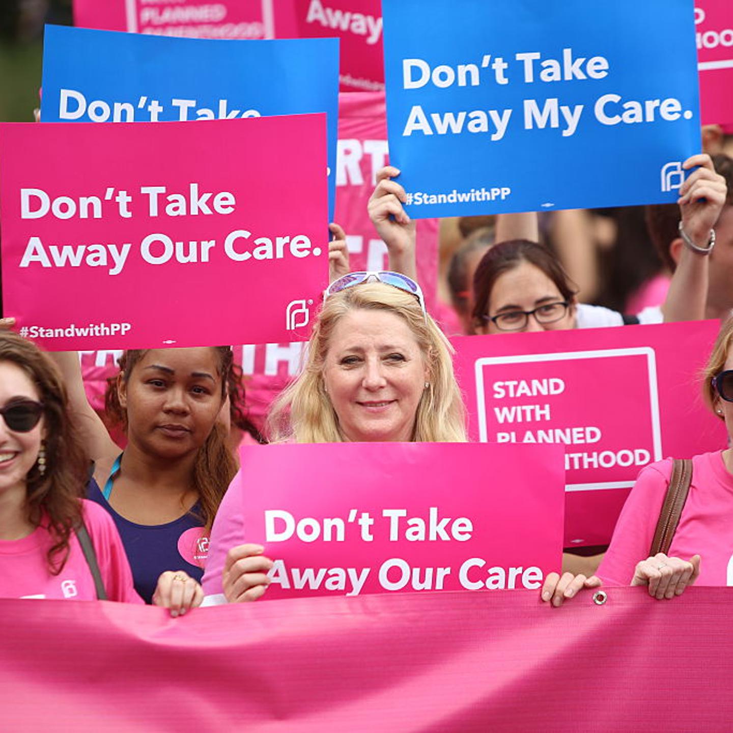 Planned Parenthood supporters hold pink banner and signs.