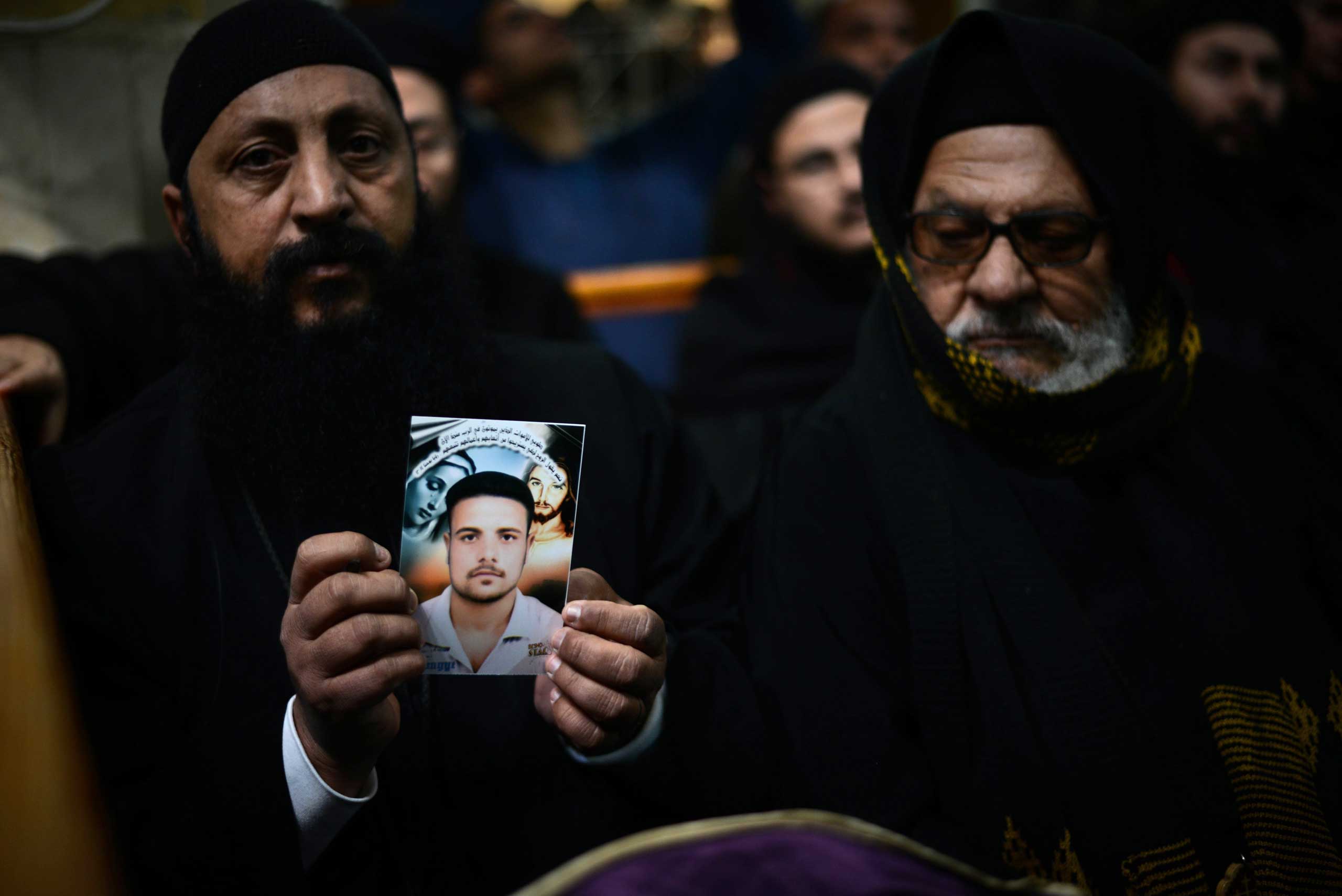 A Coptic clergyman shows a picture of a man whom he says is one of the Egyptian Coptic Christians purportedly murdered by ISIS group militants in Libya, on Feb. 16, 2015, during a memorial ceremony in the village of al-Awar in Egypt's southern province o