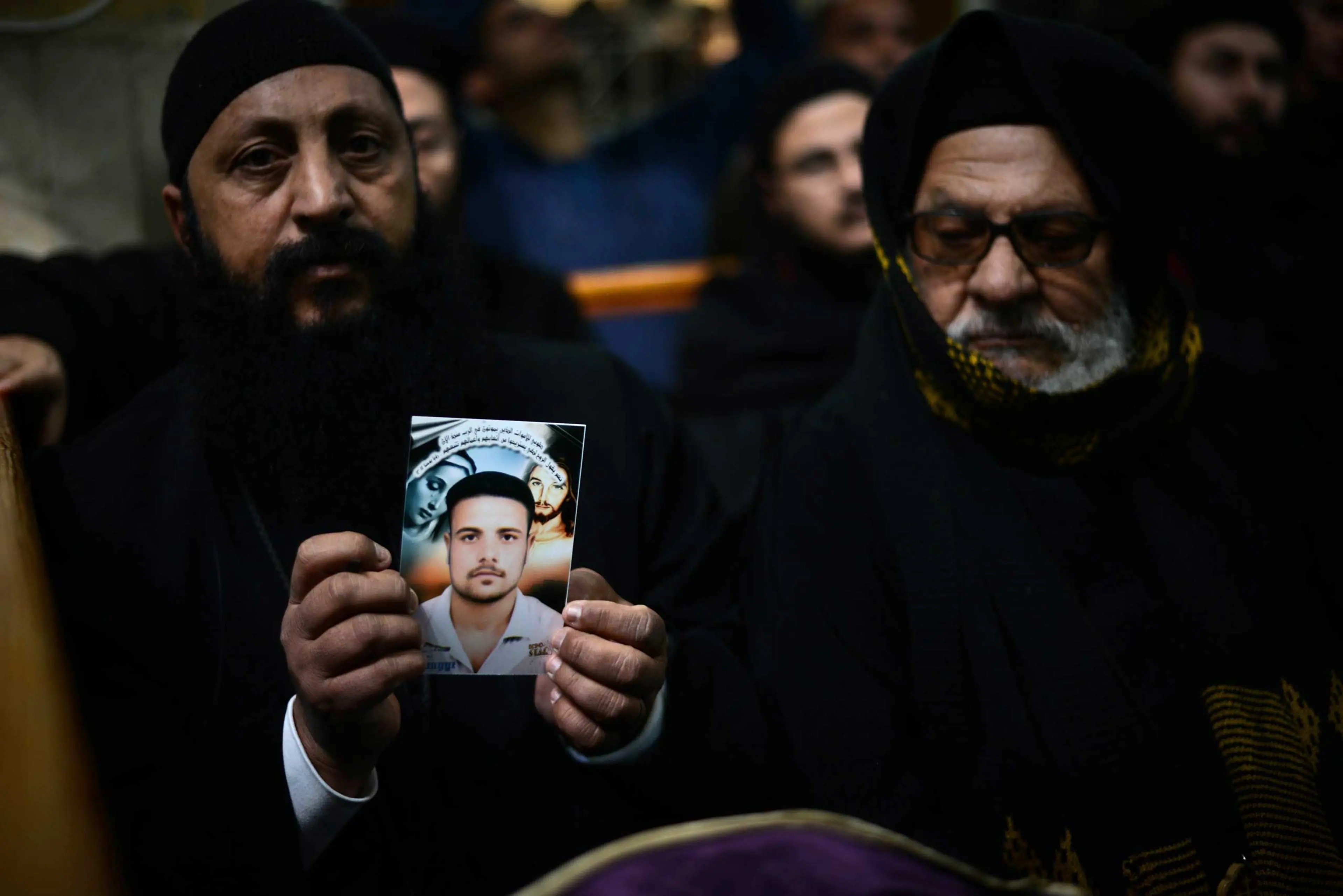 A Coptic clergyman shows a picture of a man whom he says is one of the Egyptian Coptic Christians purportedly murdered by ISIS group militants in Libya, on Feb. 16, 2015, during a memorial ceremony in the village of al-Awar in Egypt's southern province o