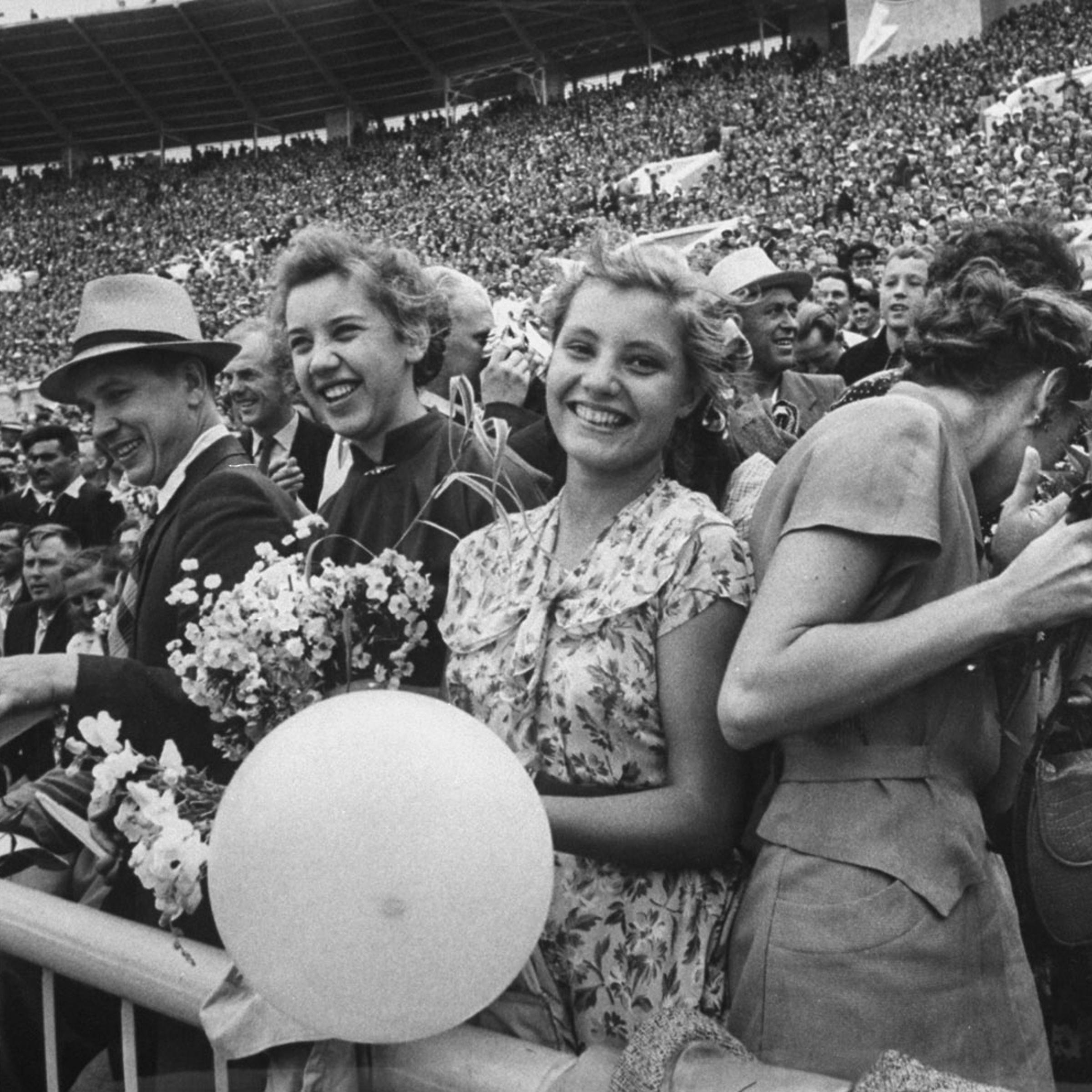 Crowd at Lenin Stadium during a sports festival, with some holding flowers for the winning athletes, 1956.