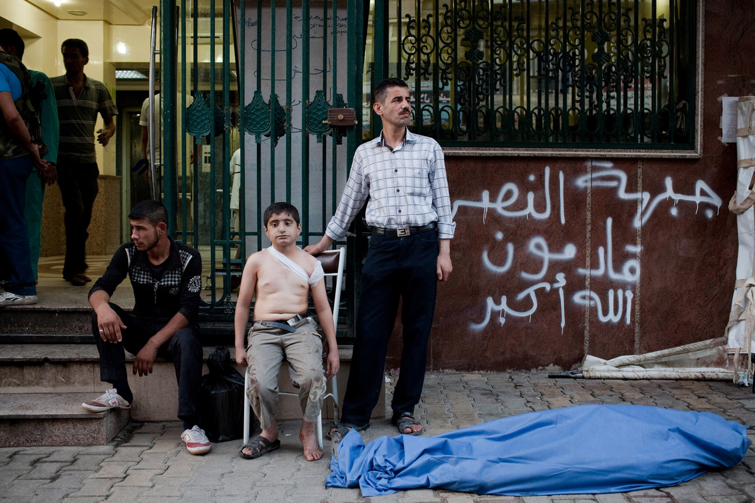 Aug. 24, 2012. Ahmed, 12, waits with his uncle (right) near the body of his father, killed by a shell in Sha'ar. Ahmed, who saw his father die, was also wounded in his back by shrapnel.