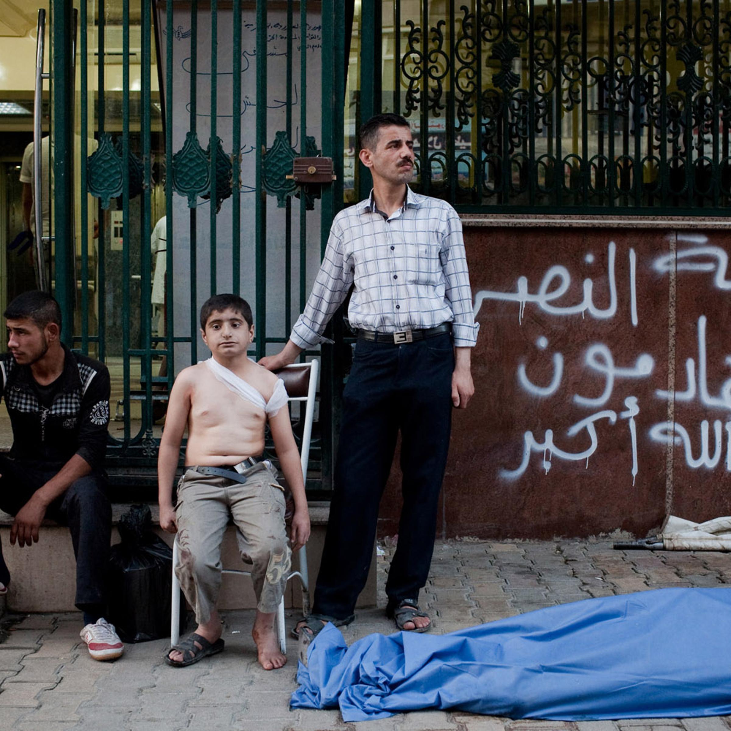 Aug. 24, 2012. Ahmed, 12, waits with his uncle (right) near the body of his father, killed by a shell in Sha'ar. Ahmed, who saw his father die, was also wounded in his back by shrapnel.