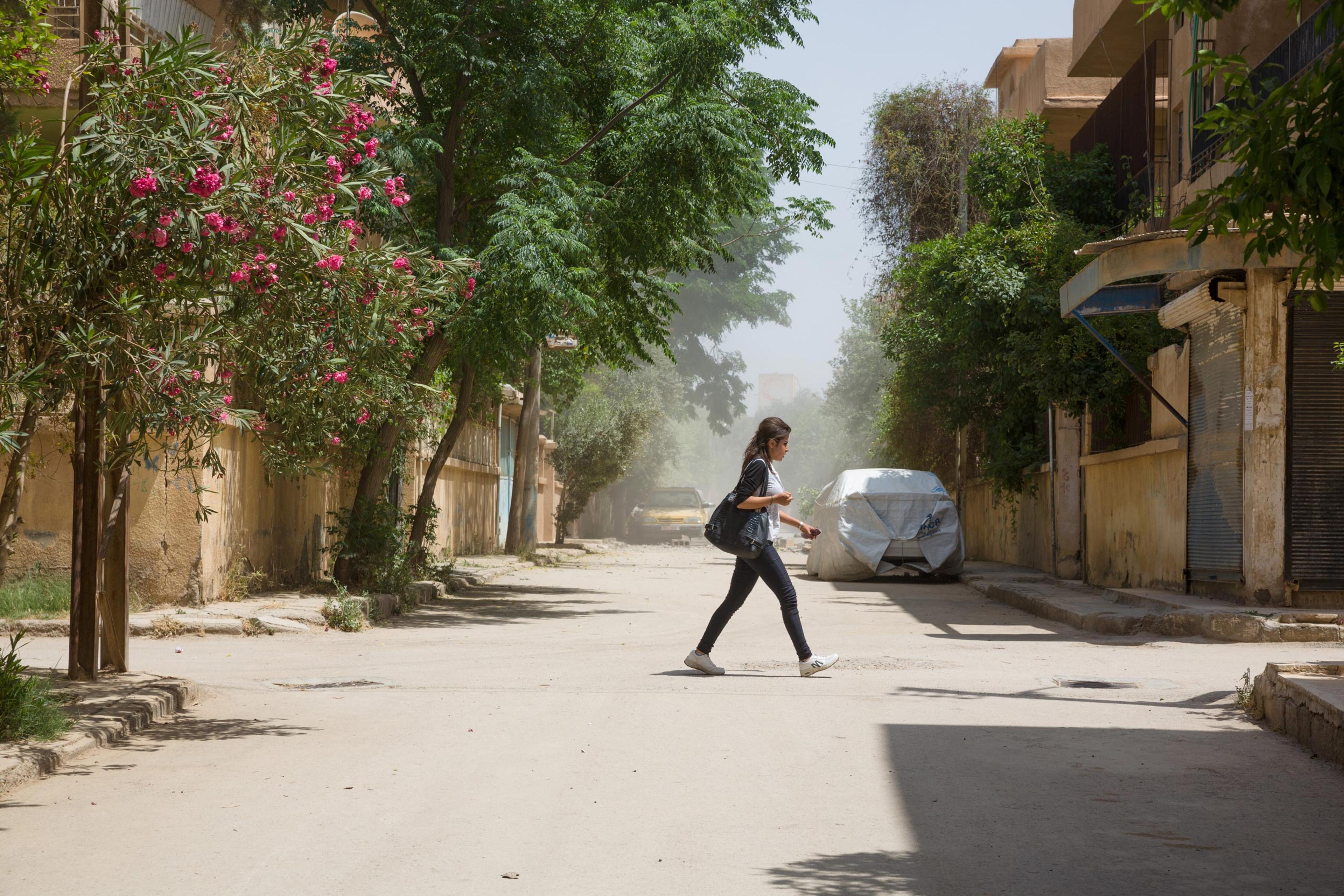 A young woman crosses a street in Ghazi Ayaash, a residential neighborhood of Deir-ez Zor a few hundred feet from the frontline, after a mortar attack from an ISIS position. The city is an outpost of modernity surrounded by ISIS-controlled areas where strict Islamic law is enforced, May 20, 2015.
