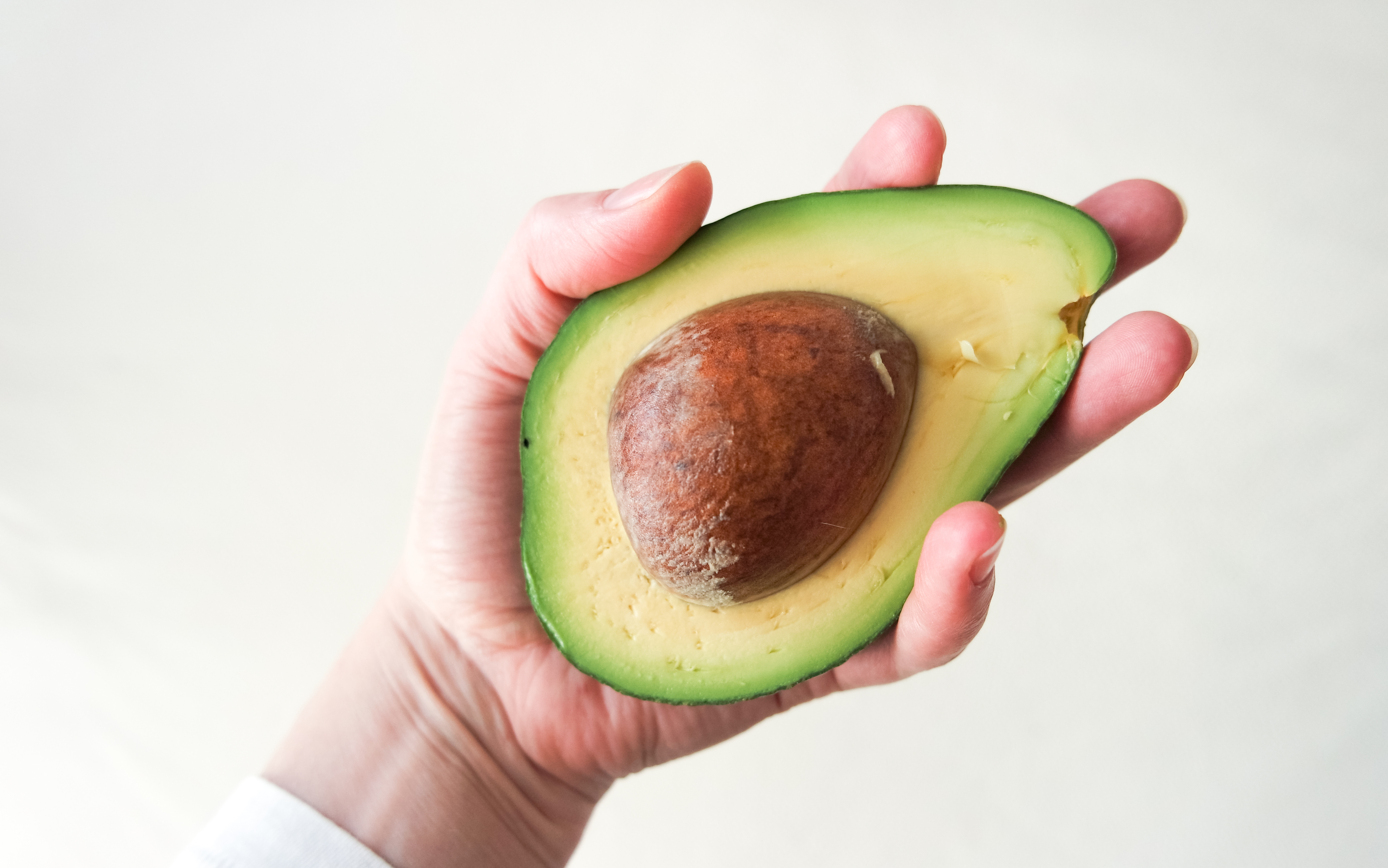 Cropped Hand Holding Avocado Against Wall