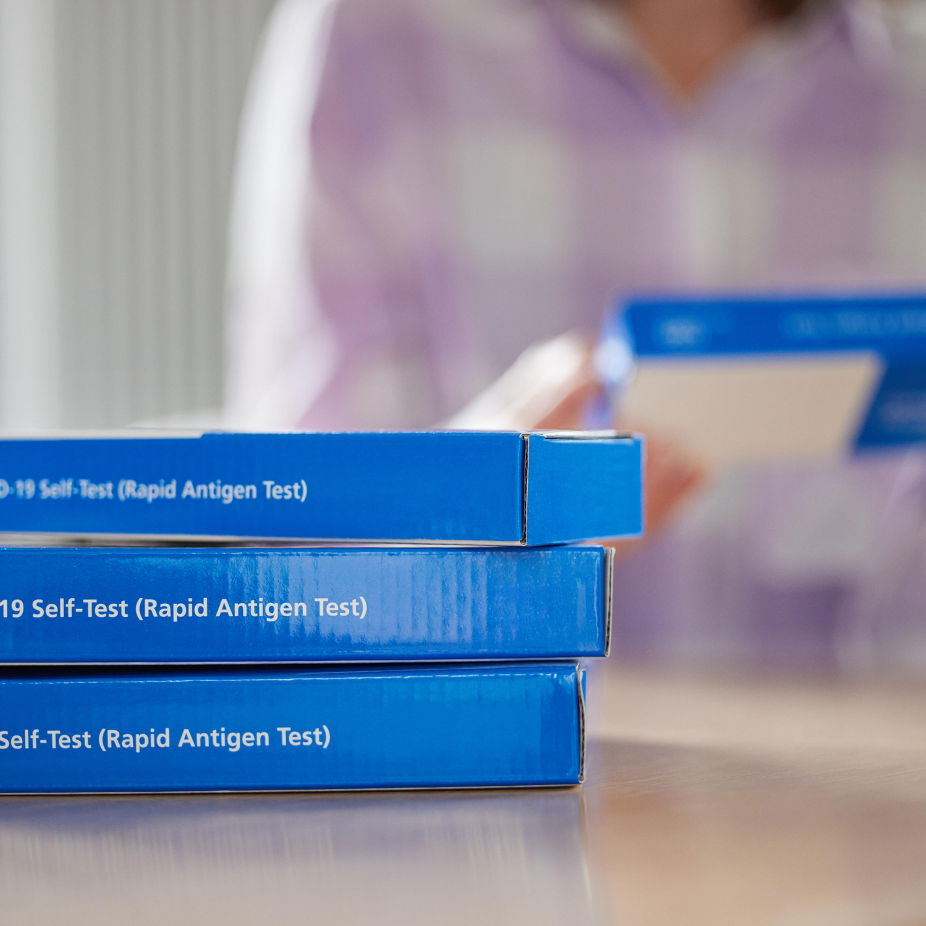 Close Up Of Woman At Home Reading Instructions On Supply Of Covid-19 Rapid Antigen Self-Testing Kits