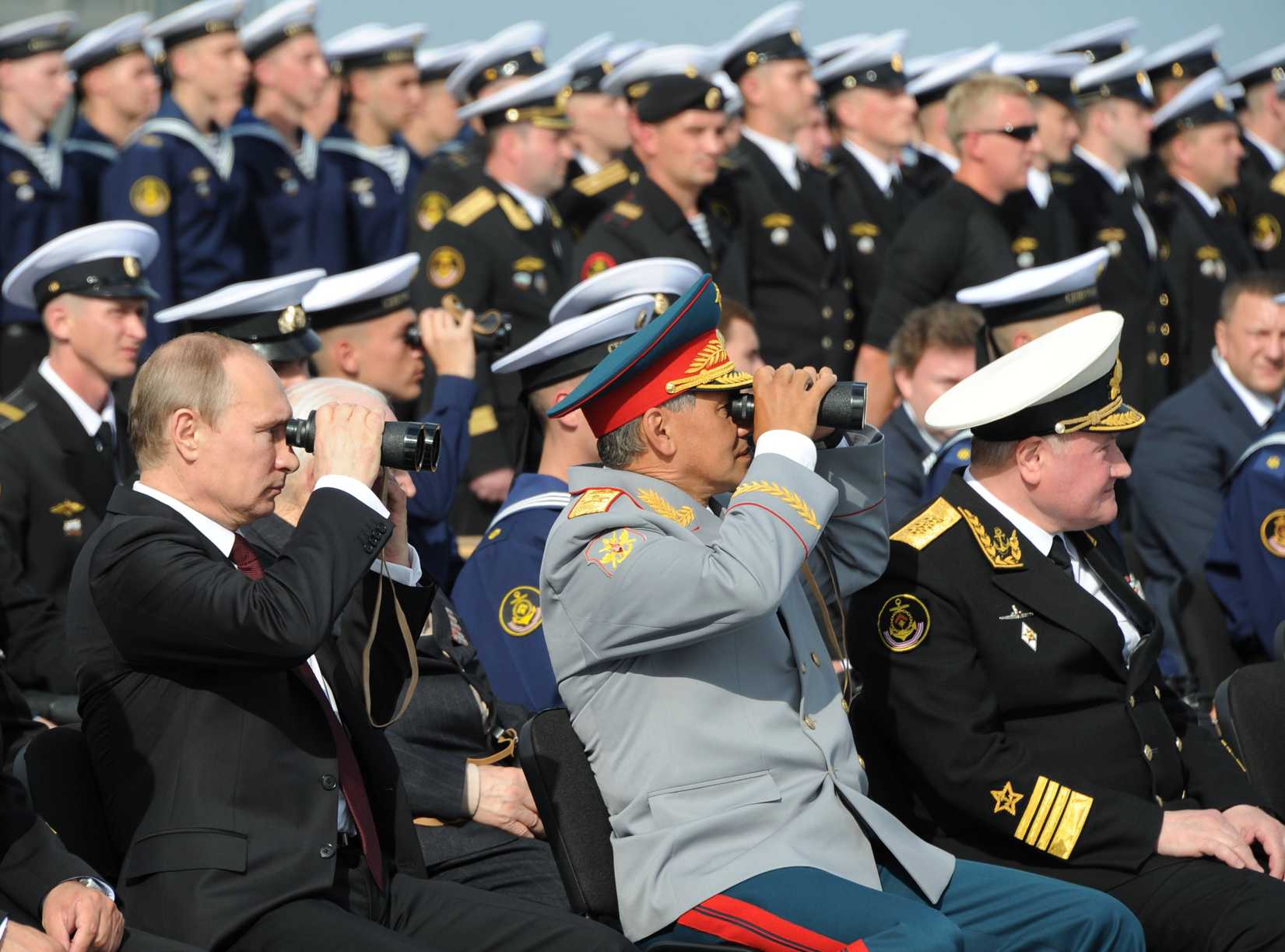 Russian President Vladimir Putin, left, and Russian Defense Minister Sergei Shoigu, center, use binoculars to watch a parade marking the country's Navy Day in Severomorsk, Russia, In this Sunday, on July 27, 2014 