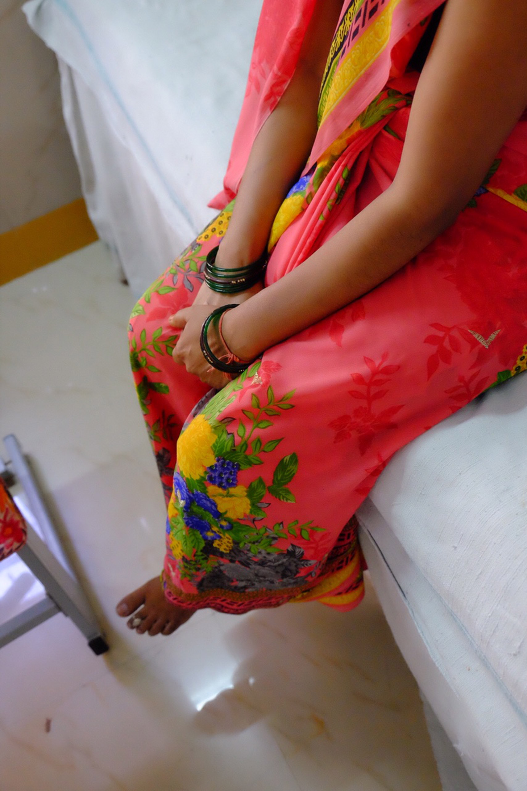 A woman sitting on a bed at an Udaipur hospital, waiting for an IUD insertion.