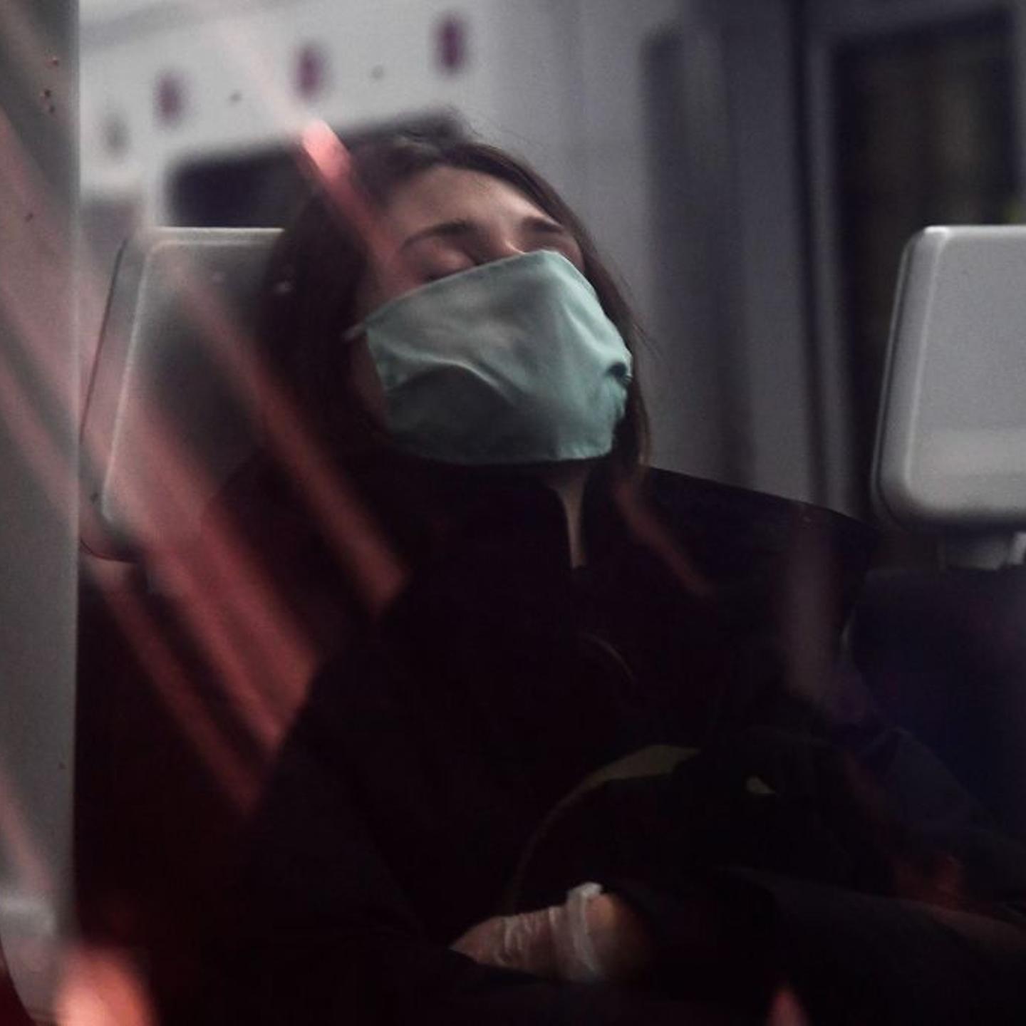 A woman wearing a face mask sleeps on a train at the Atocha Station in Madrid on April 13, 2020.