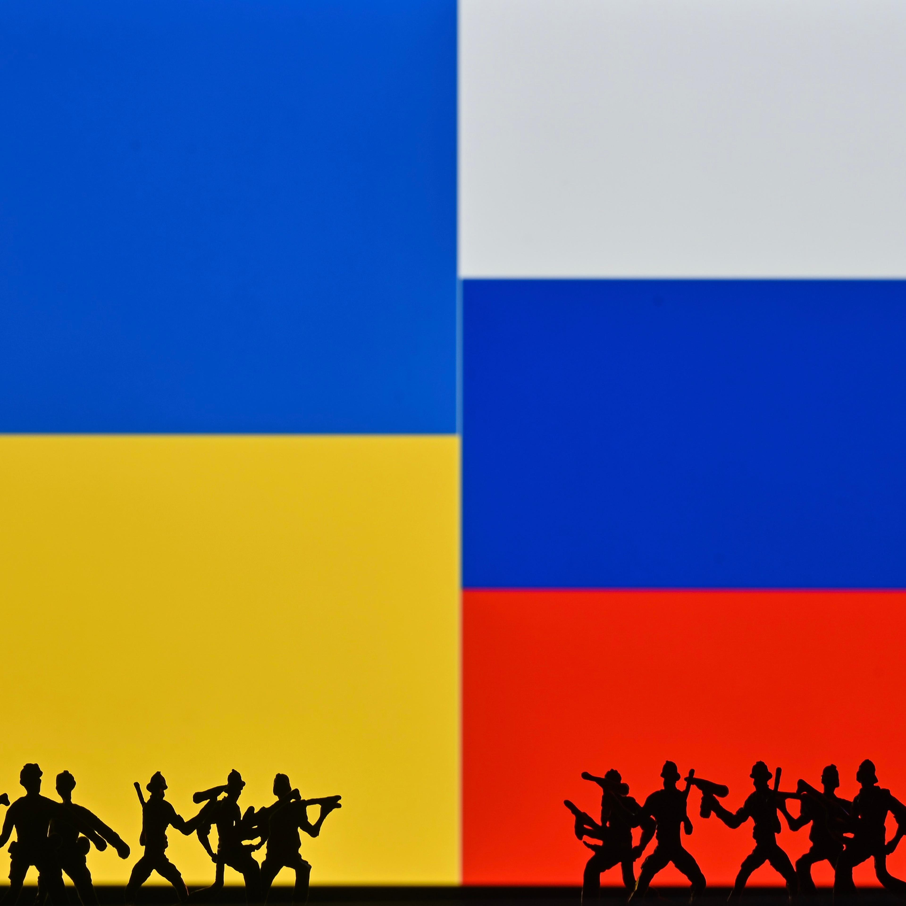 Illustrative photo of small figures of soldiers representing two armies in front of the flags of Ukraine and Russia
