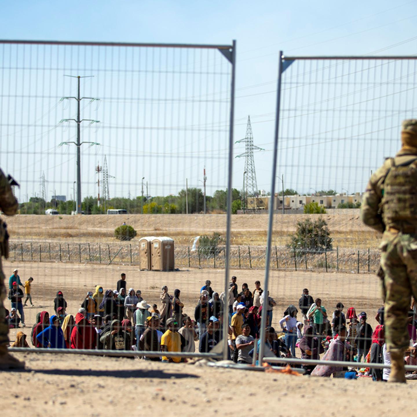 Migrants wait in line adjacent to the border fence under the watch of the Texas National Guard to enter into El Paso, Texas, May 10, 2023.