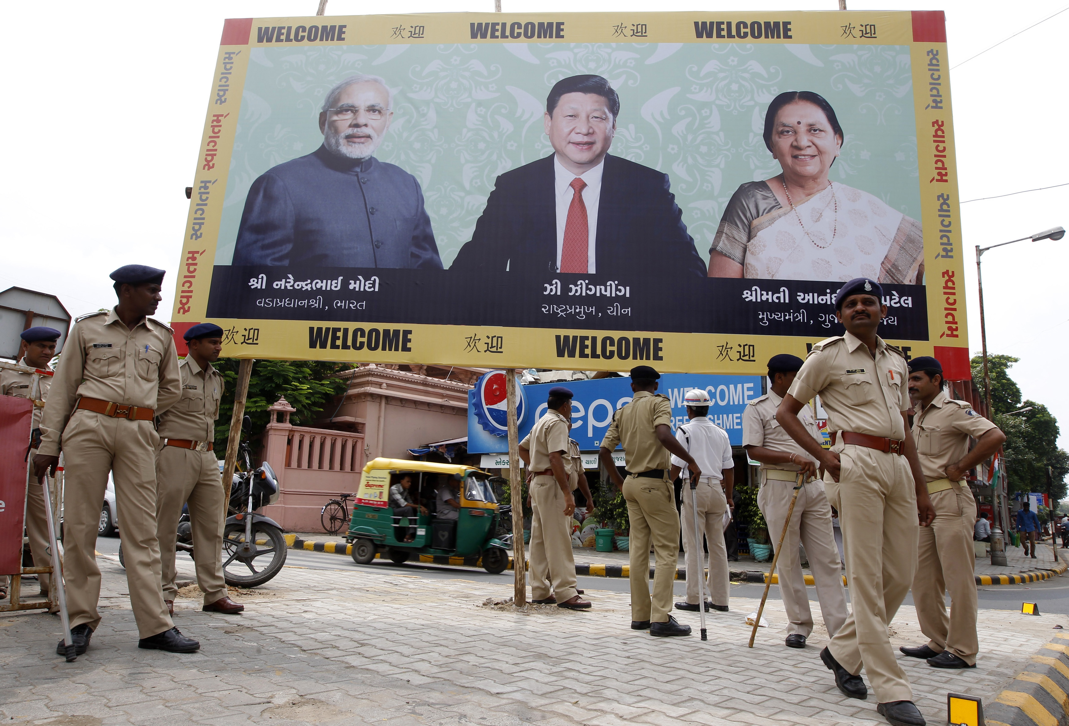 Police personnel stand guard in front of a boarding with images of India's PM Modi, China's President Xi and Patel, Chief Minister of Gujarat, ahead of Xi's arrival in Ahmedabad