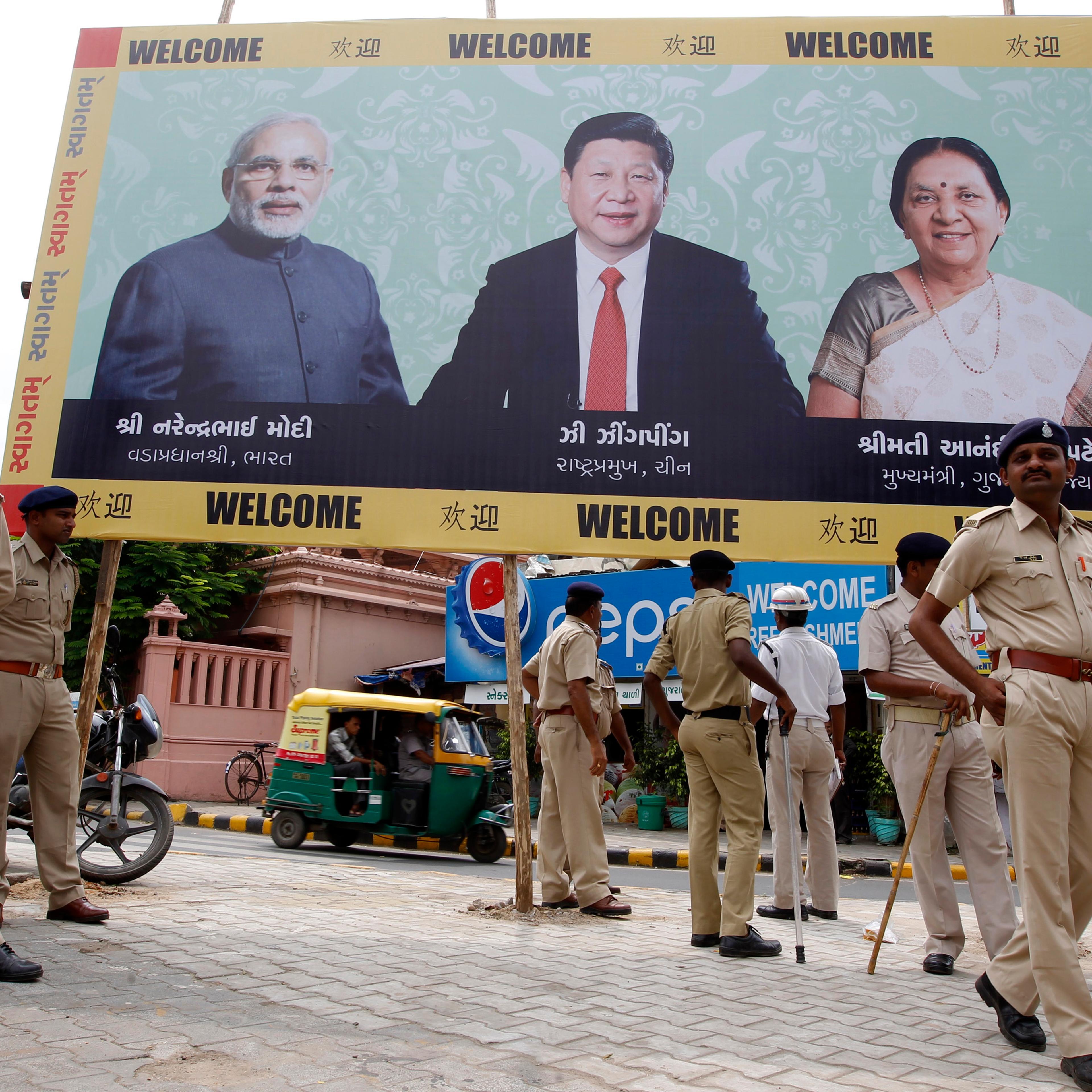 Police personnel stand guard in front of a boarding with images of India's PM Modi, China's President Xi and Patel, Chief Minister of Gujarat, ahead of Xi's arrival in Ahmedabad