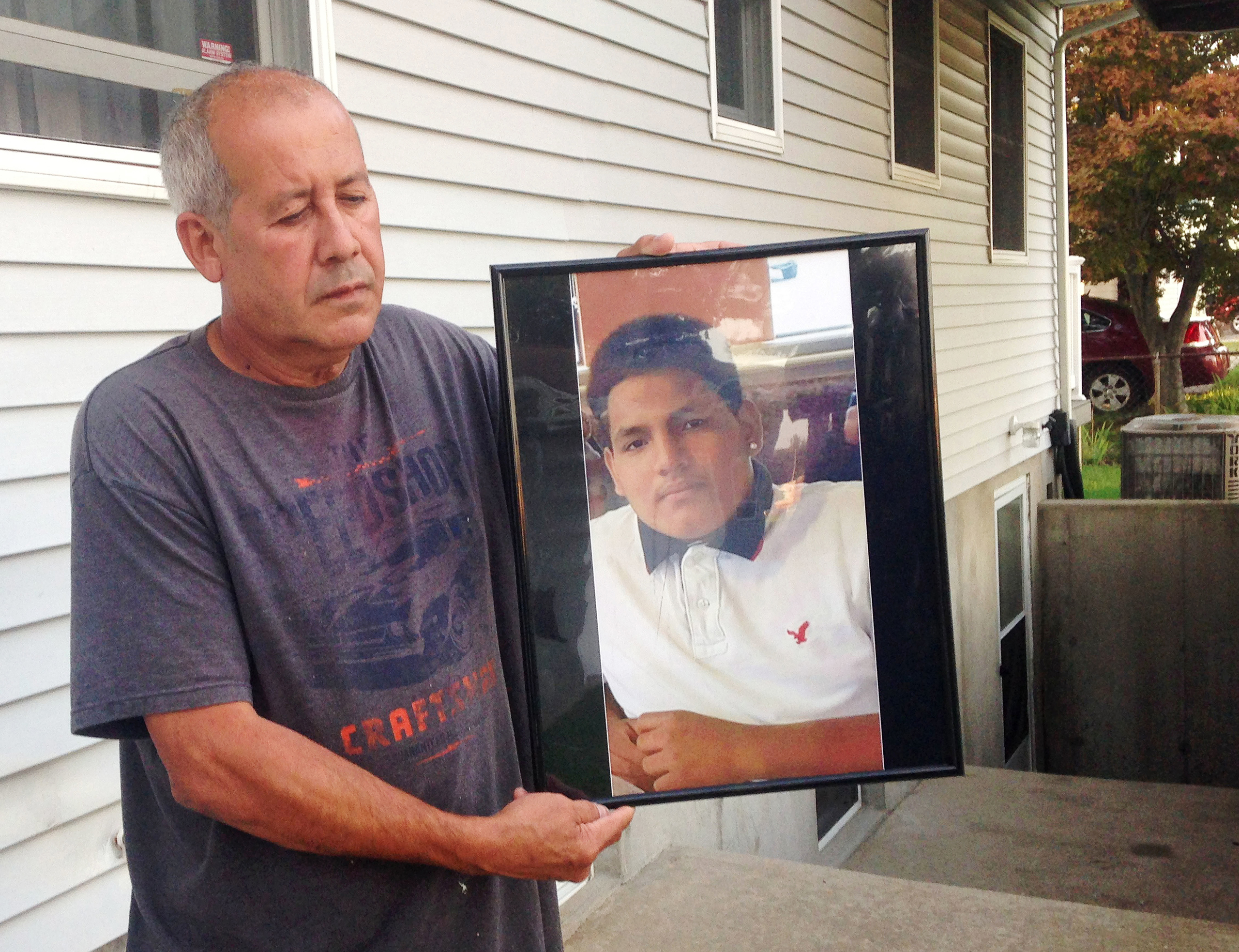 In this Sept. 27, 2016 photo, Abraham Chaparro, holds a photograph of his murdered stepson, Miguel Garcia-Moran, outside his home in Brentwood, N.Y. The remains of Garcia-Moran, who was reported missing in February, were found in September. Multiple teen
