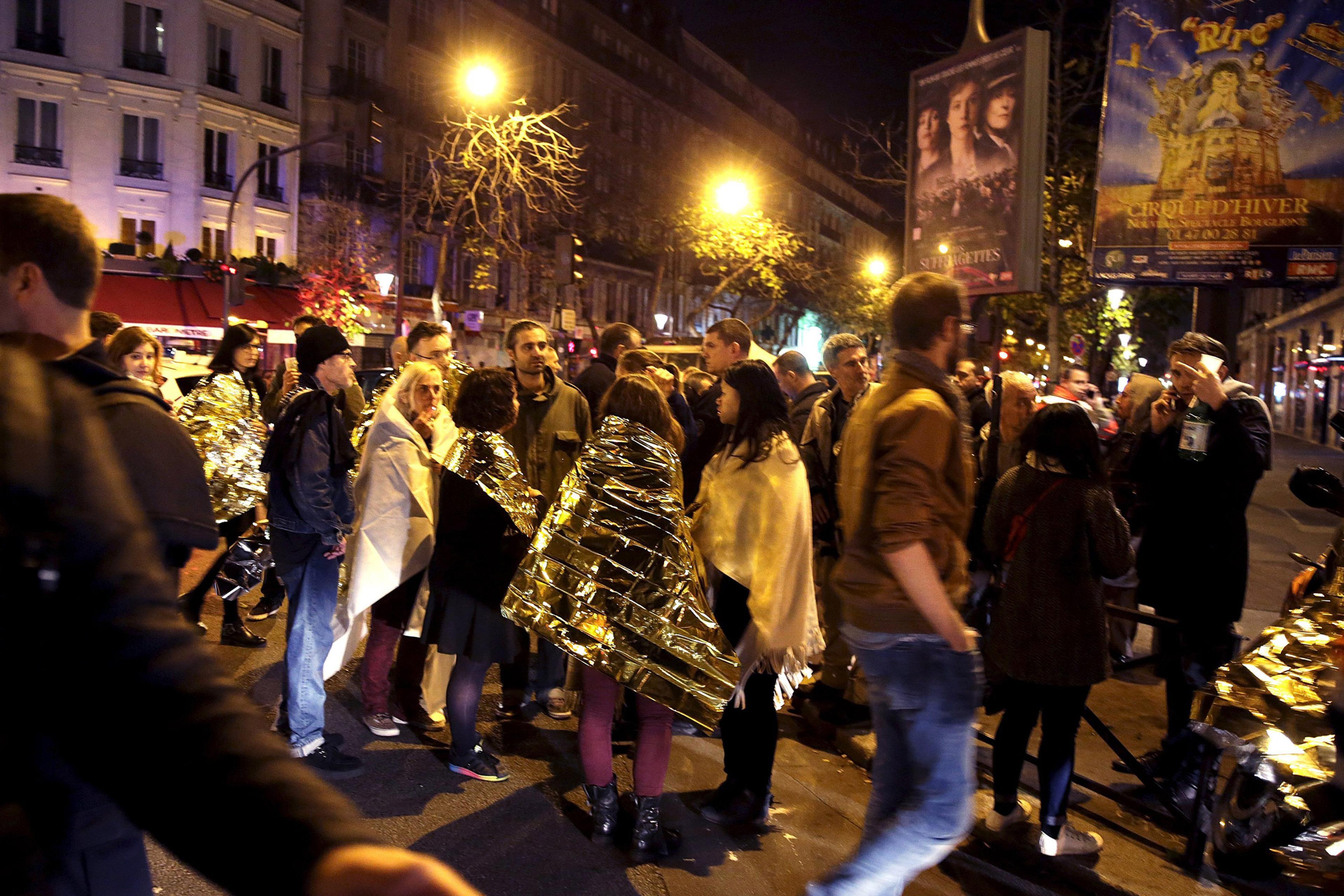 People warm up under protective thermal blankets as they gather on a street near the Bataclan concert hall following fatal attacks in Paris, France