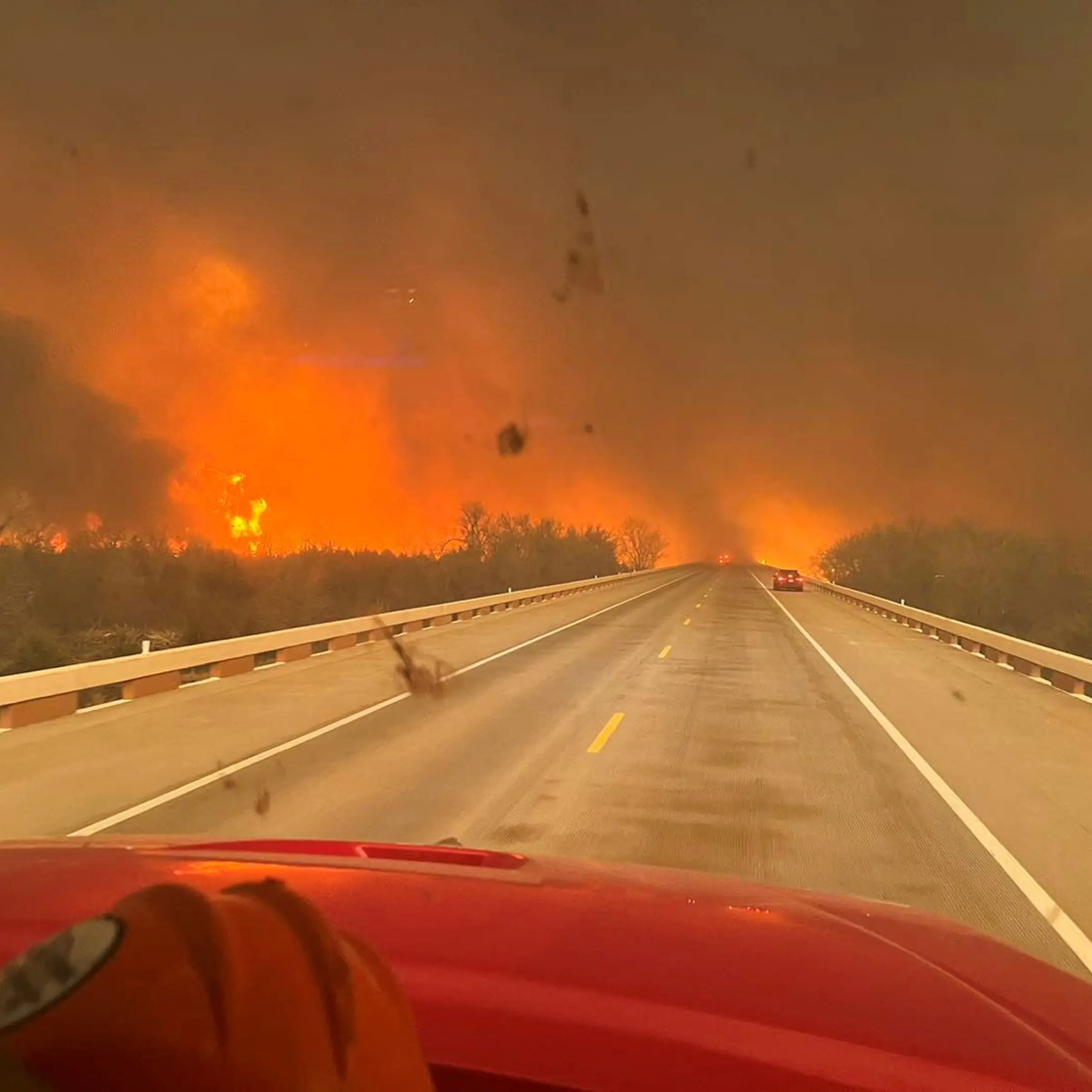 Cars drive as smoke and fire rise from wildfires in Texas
