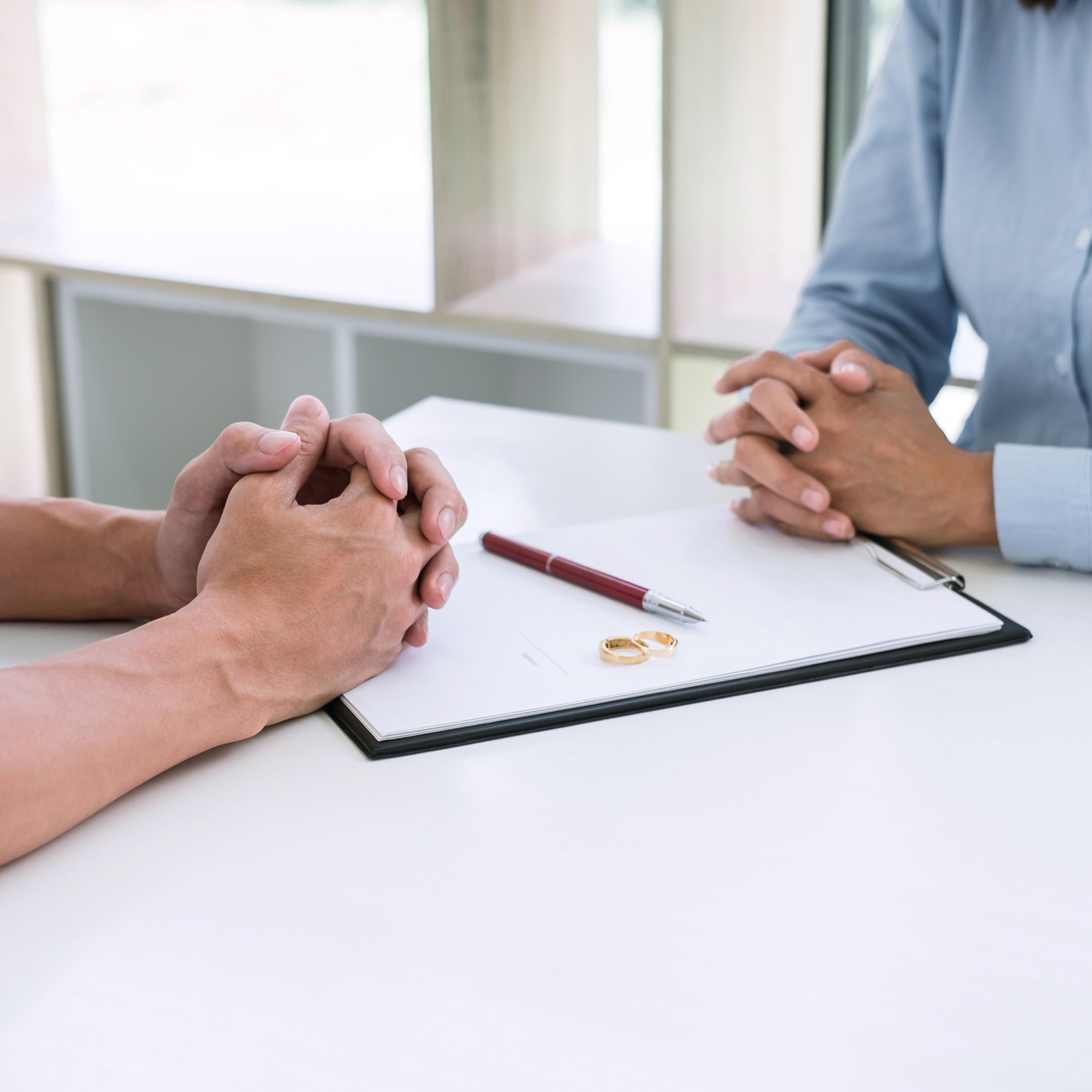 Midsection Of Couple With Divorce Paper And Wedding Rings On Table