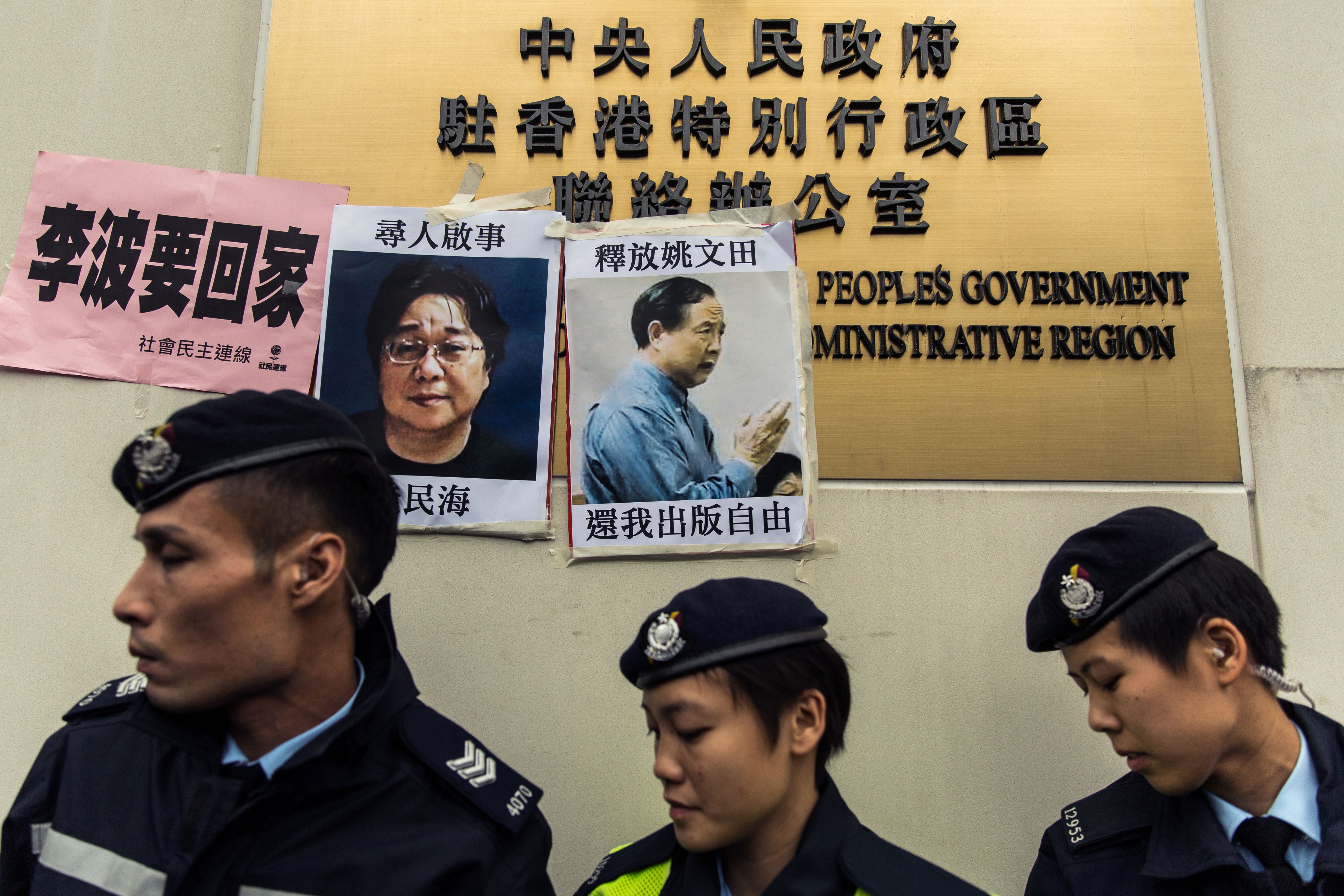 Police walk past missing-person notices for Gui Minhai, left, one of five missing booksellers from the Mighty Current publishing house, and Yau Wentian, a Hong Kong publisher who was jailed for 10 years in 2015 while preparing to release a book critical 