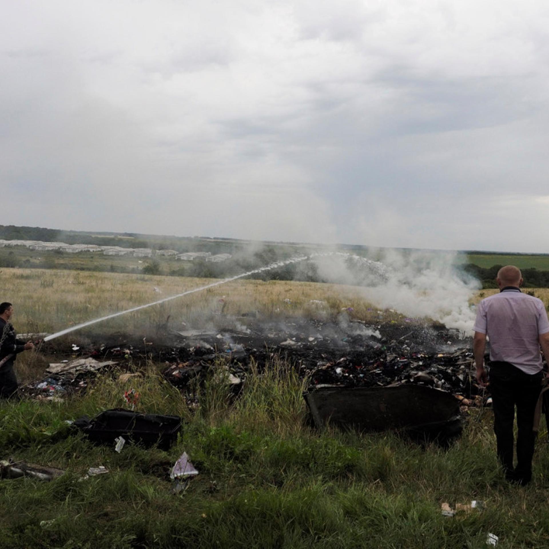 A firefighter and an armed man look at the remains and the corpses of passengers aboard Malaysia Airlines flight MH17 that was shot down over eastern Ukraine, July 17, 2014.