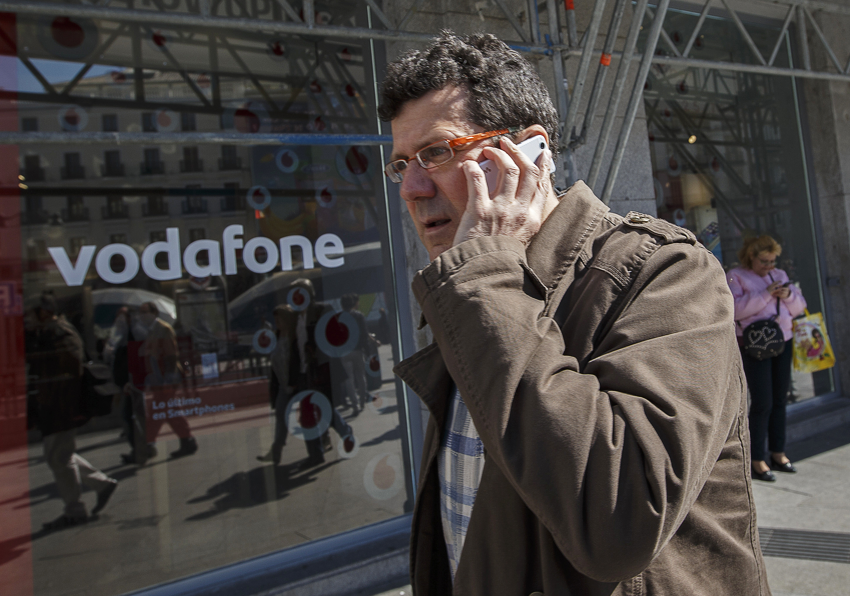 A man talking on a mobile phone walks past a Vodafone store in central Madrid