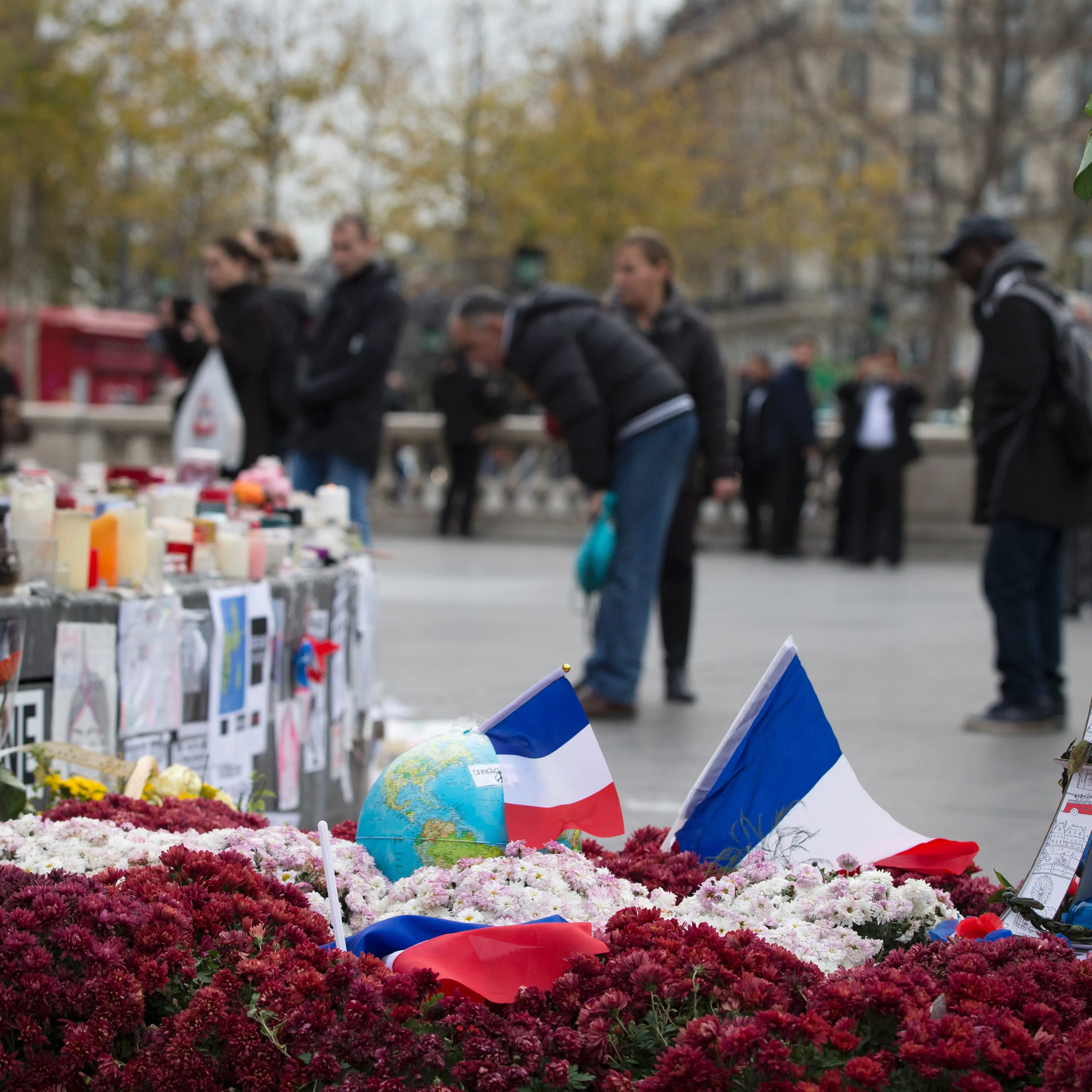 People stand on the Place de la Republique in Paris on December 2, 2015, next to a model Eiffel Tower, flowers and French flags layed in memory of the victims of the deadly attacks in and around Paris on Nov. 13.