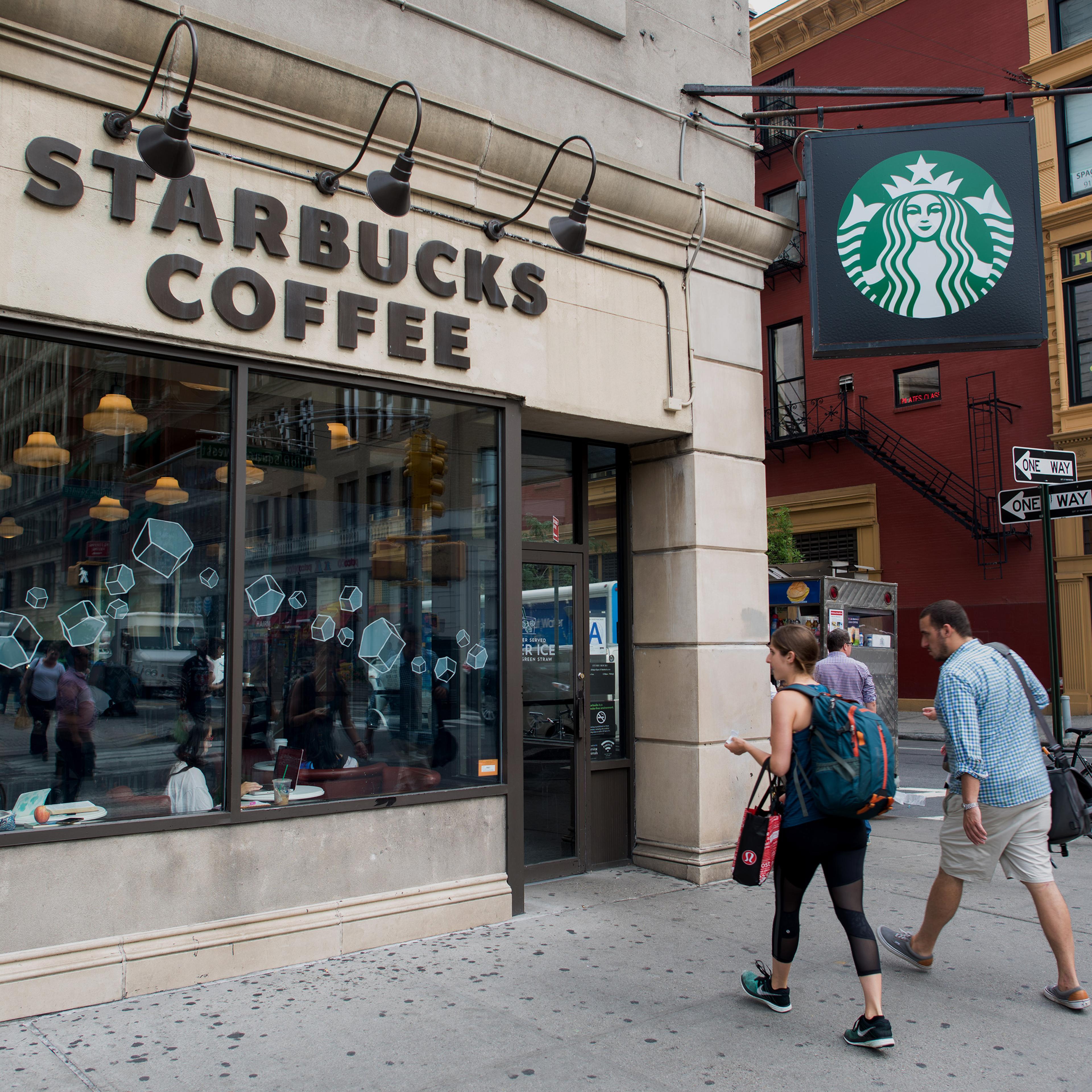 Pedestrians stroll by a Starbucks Coffee shop on the corner of Broadway and East 17th Street in Union Square in New York, New York, U.S., on Tuesday, July 21, 2015. Photographer: Craig Warga/Bloomberg *** Local Caption ***
