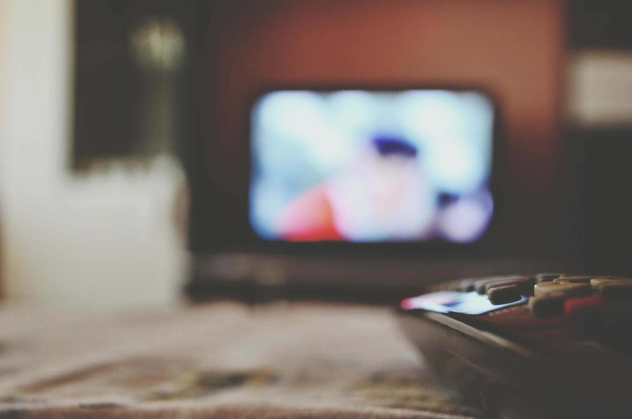 Close-up of remote control with blurred television in distance