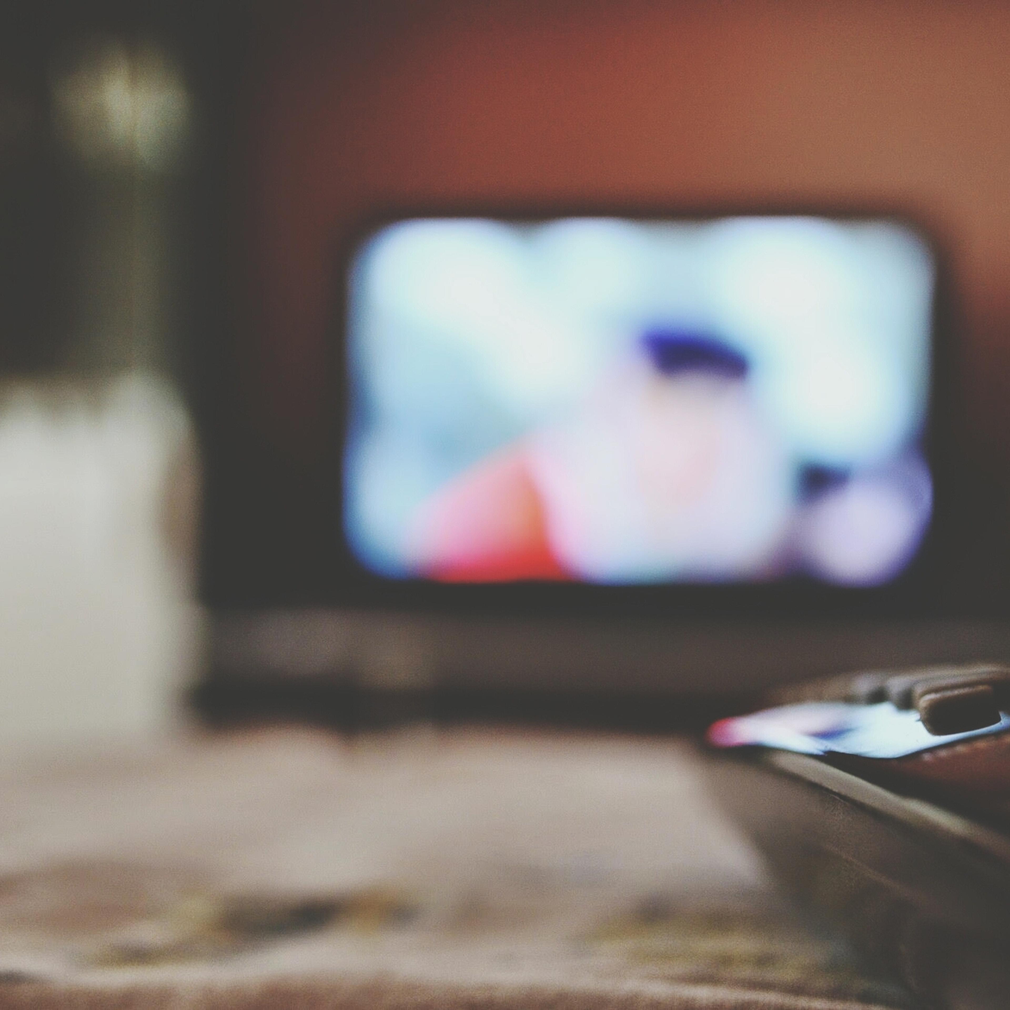 Close-up of remote control with blurred television in distance