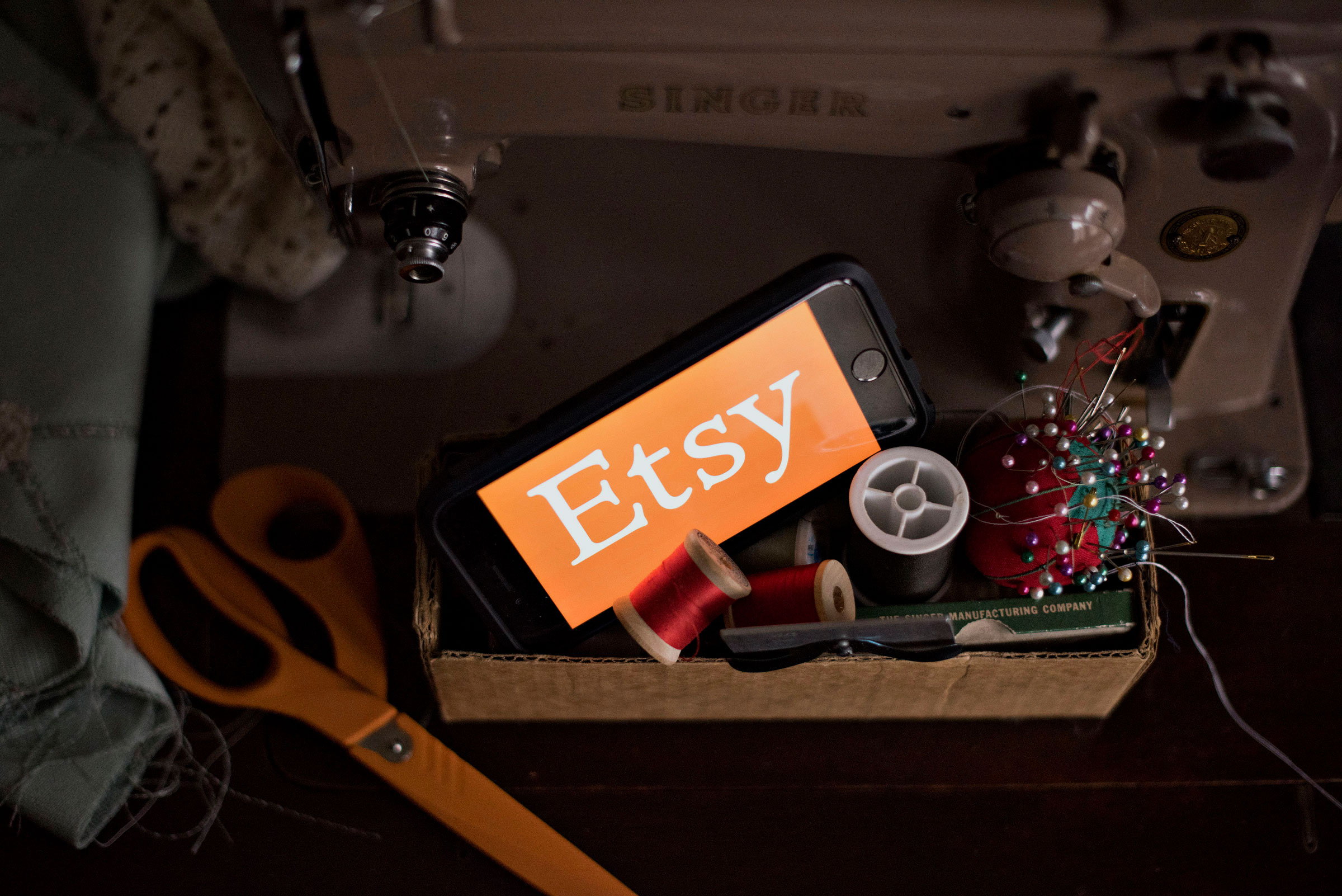 The Etsy Inc. logo is displayed for a photograph on a smartphone next to sewing supplies