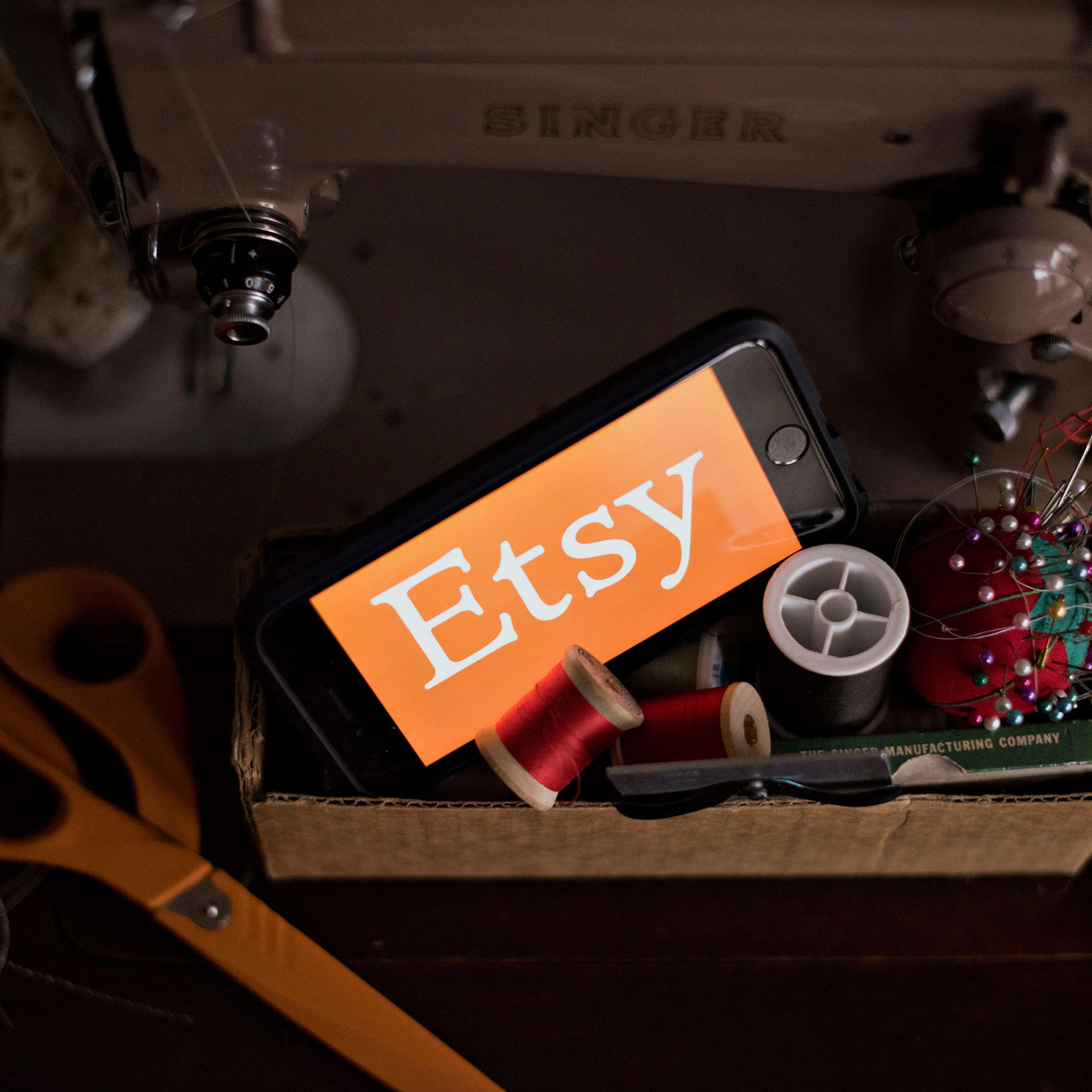 The Etsy Inc. logo is displayed for a photograph on a smartphone next to sewing supplies