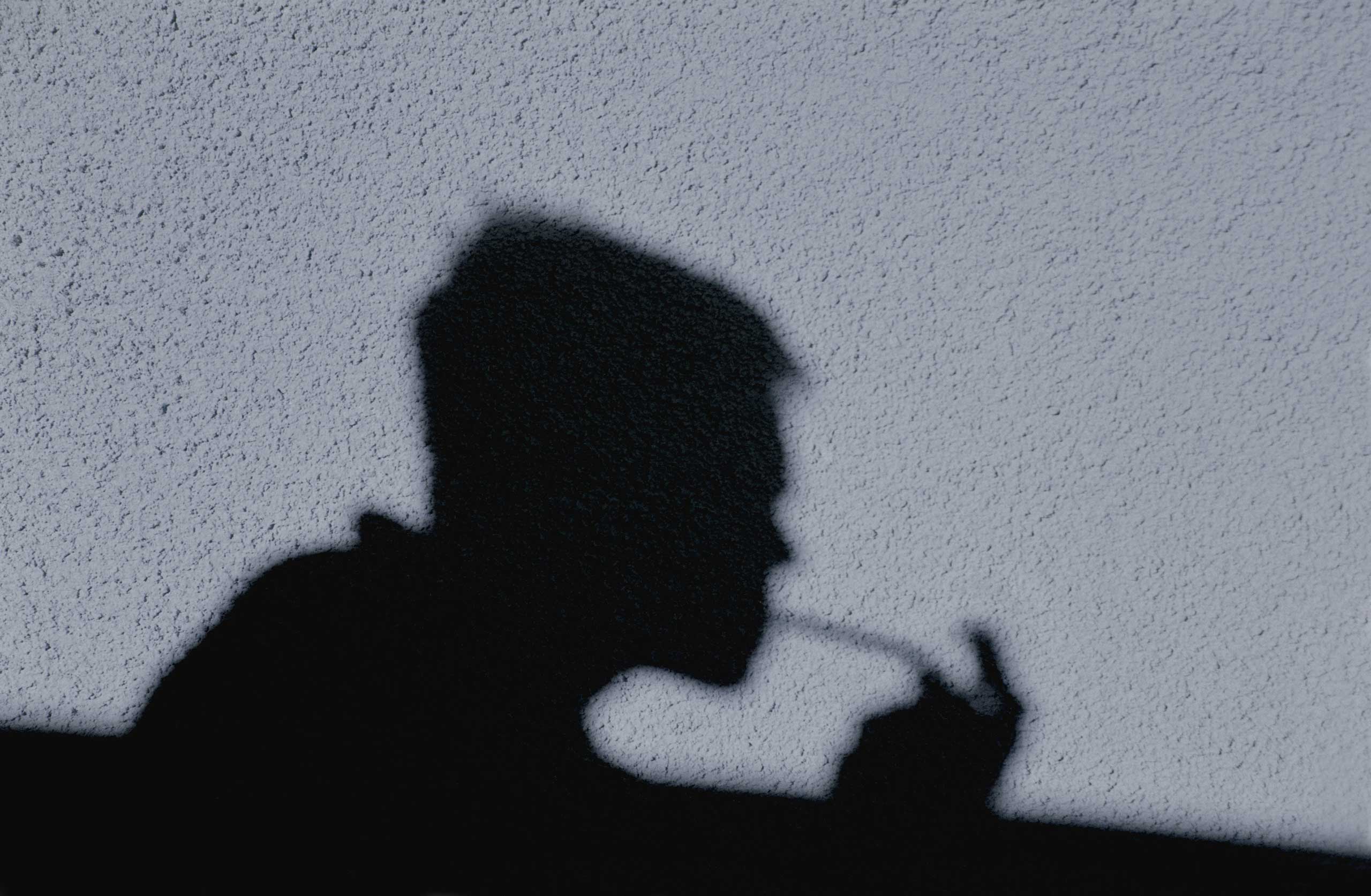 Shadow of man smoking crack cast on wall, side view