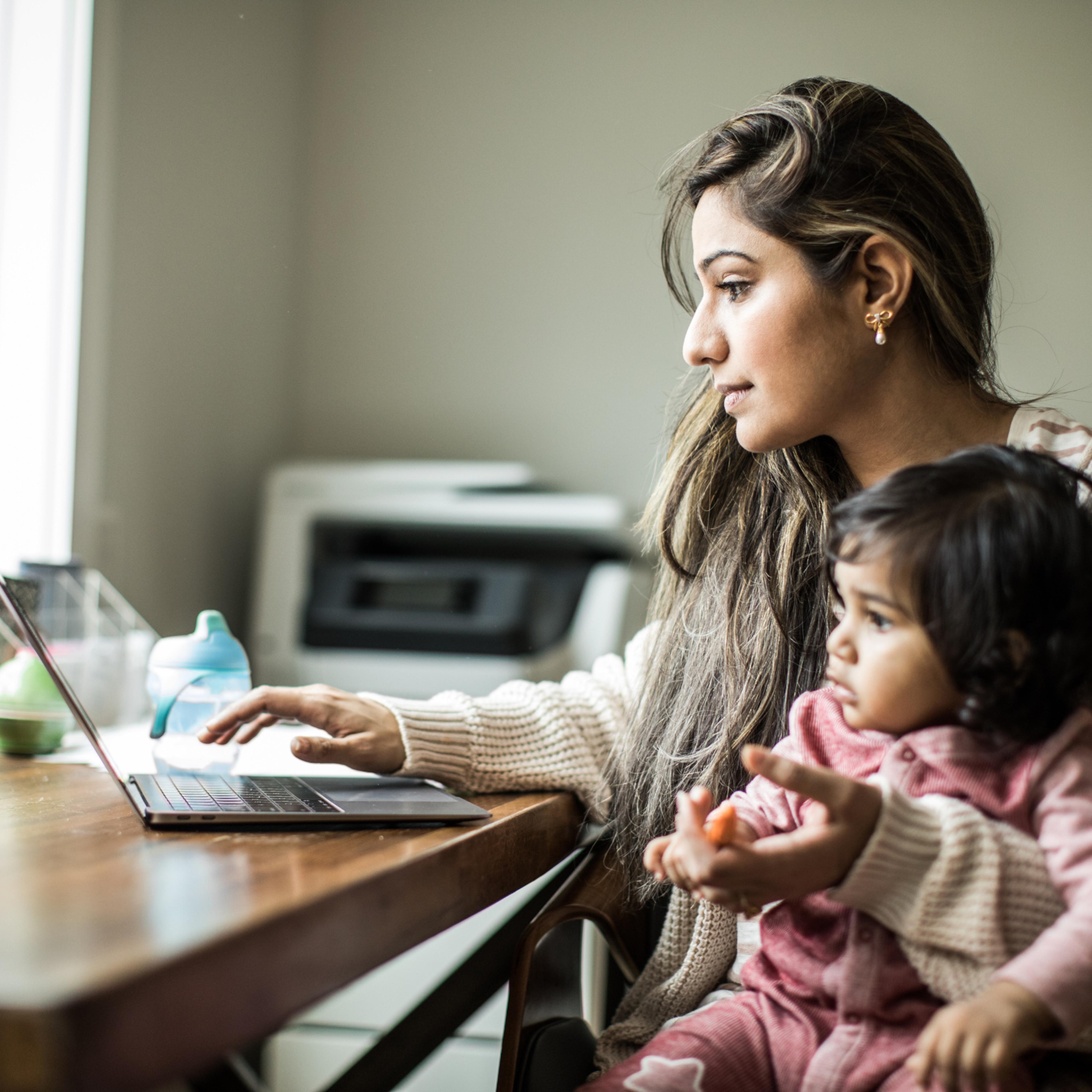 Mother multi-tasking with infant daughter in home office
