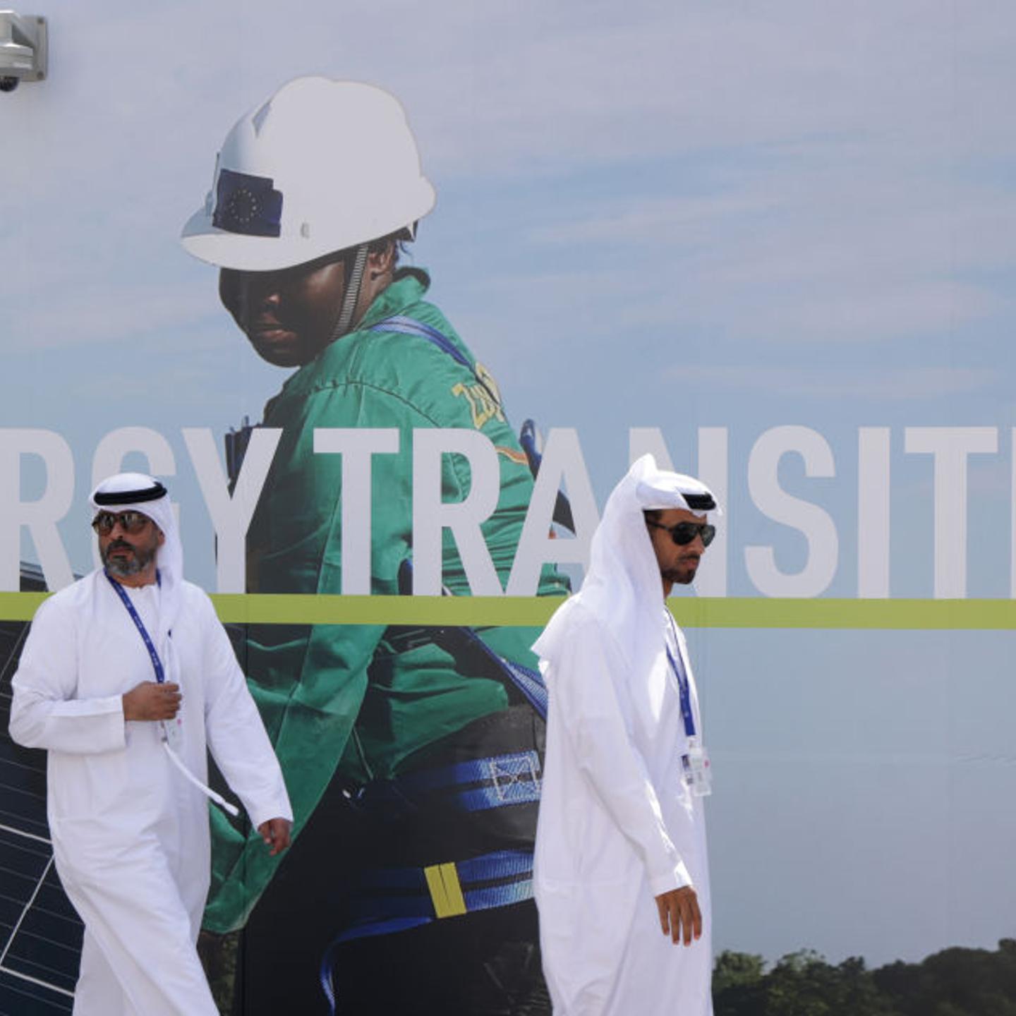 Men wearing thawbs walk past a billboard promoting the transition to renewable energies at the UNFCCC COP28 Climate Conference in Dubai, United Arab Emirates.