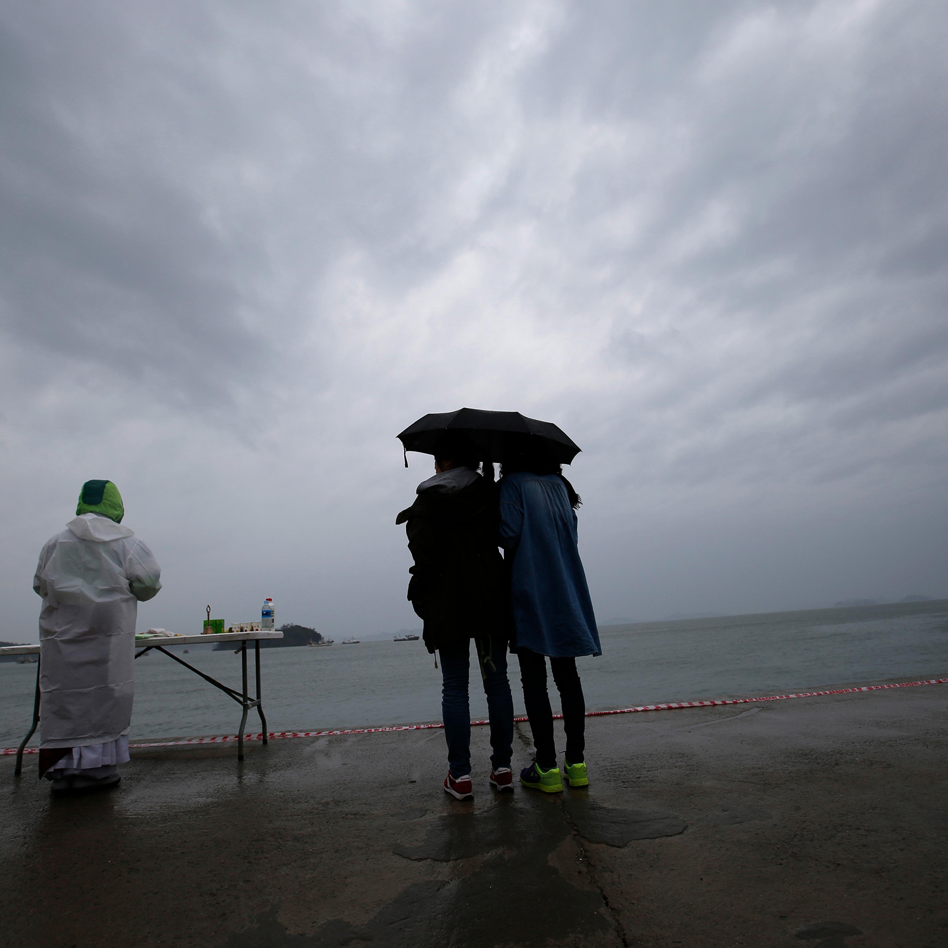 Relatives of a missing passenger onboard the capsized Sewol ferry, looks at the sea while a Buddhist monk prays for the victims at a port in the rain in Jindo