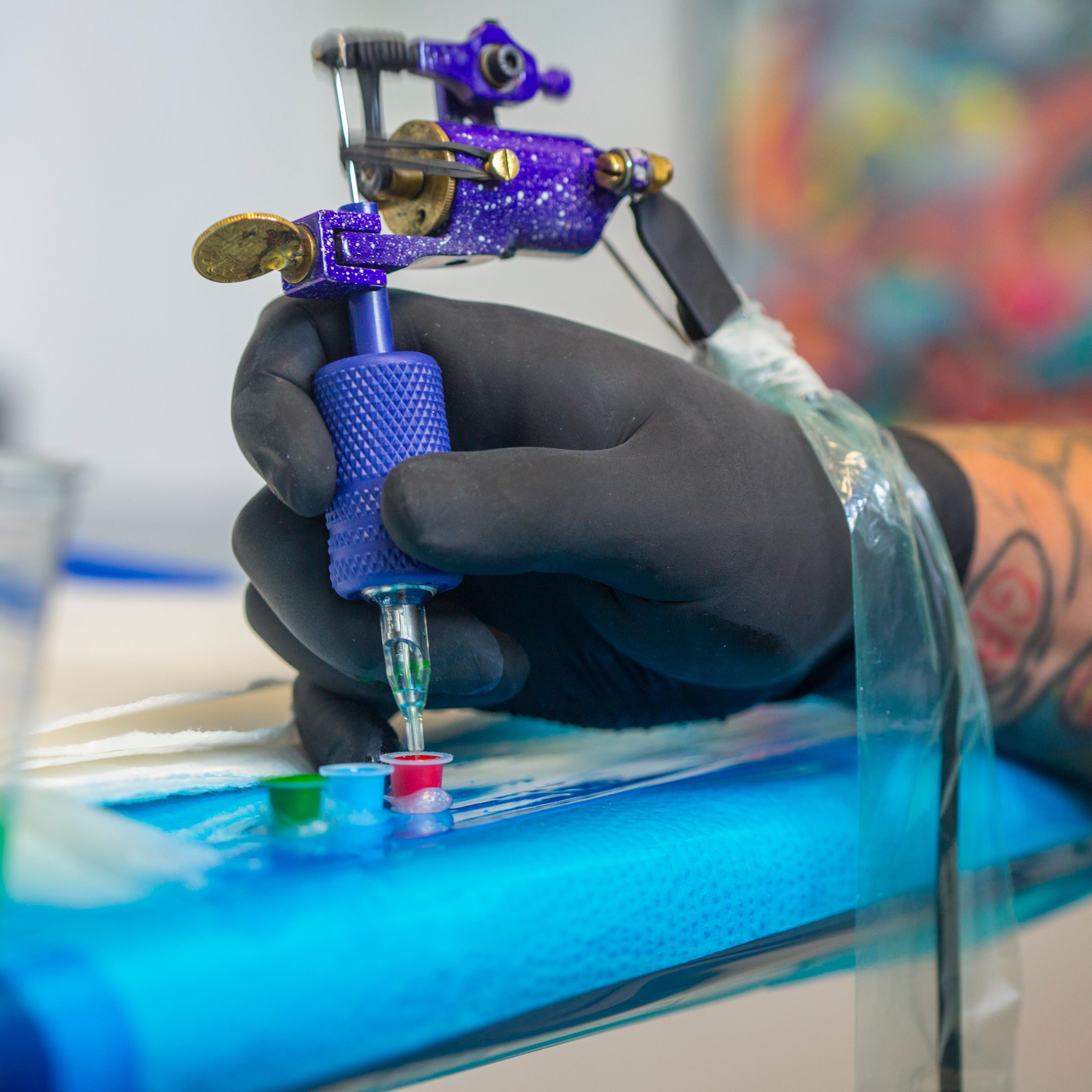 Close up of tattooist hand dipping tattoo gun's needle into red ink