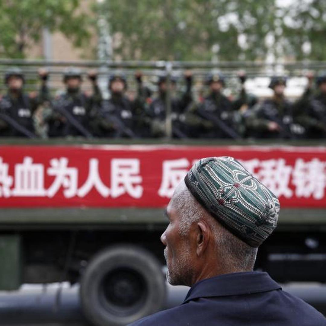 A Uighur man looks on as a truck carrying paramilitary policemen travel along a street during an anti-terrorism oath-taking rally in Urumqi