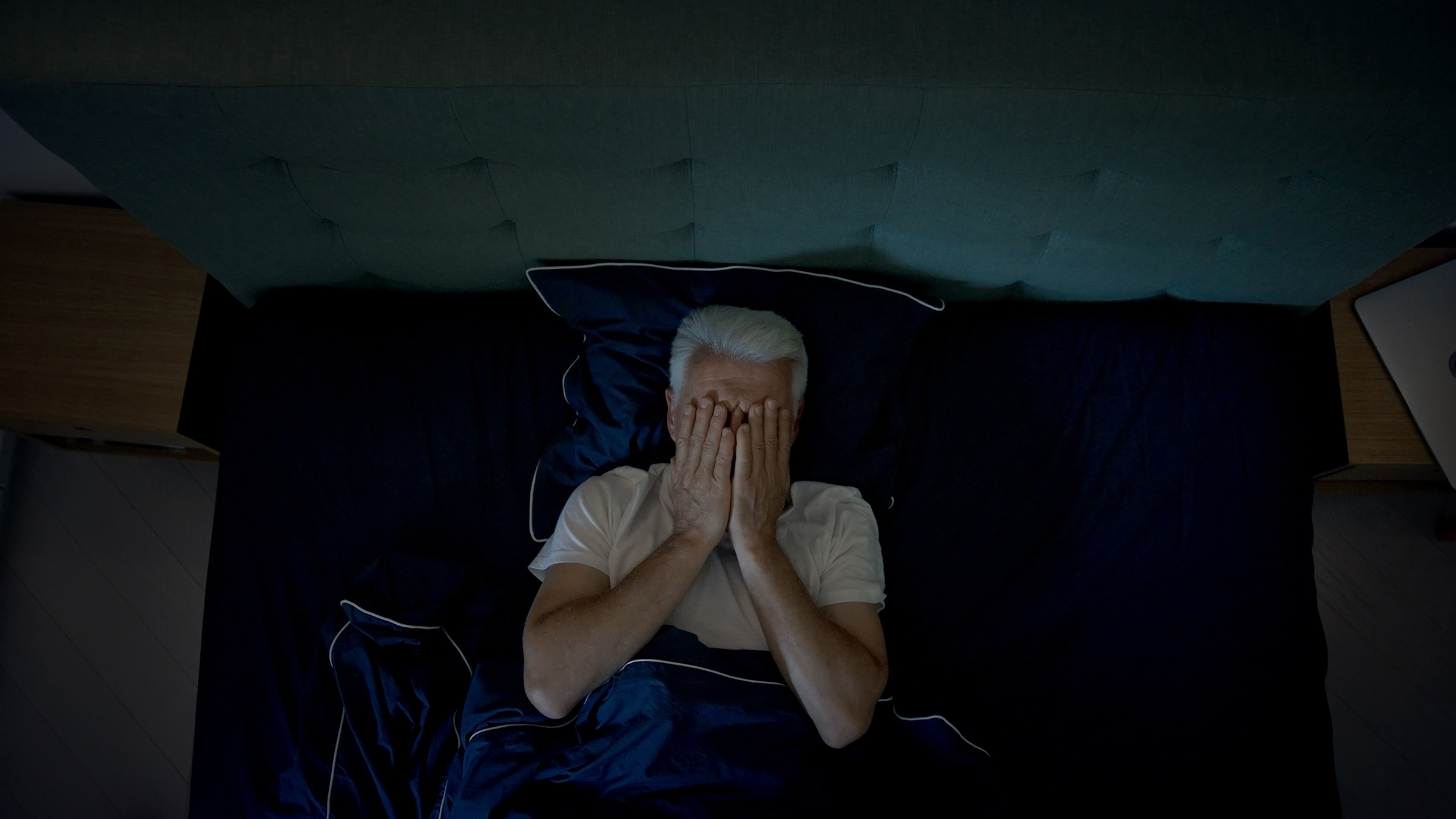 Anxious, mature man trying to sleep at night. Dealing with sleeping disorder, head in hands
