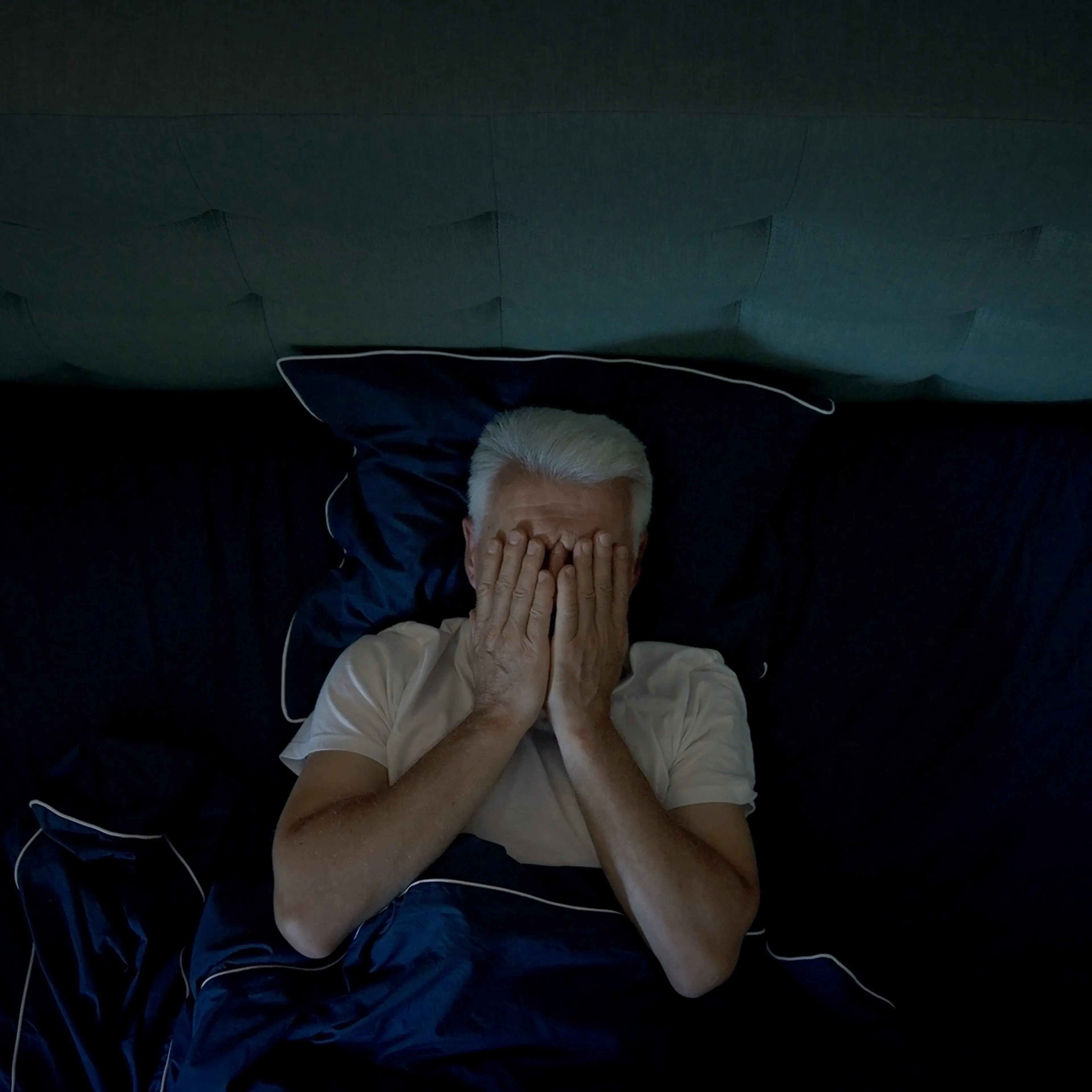 Anxious, mature man trying to sleep at night. Dealing with sleeping disorder, head in hands