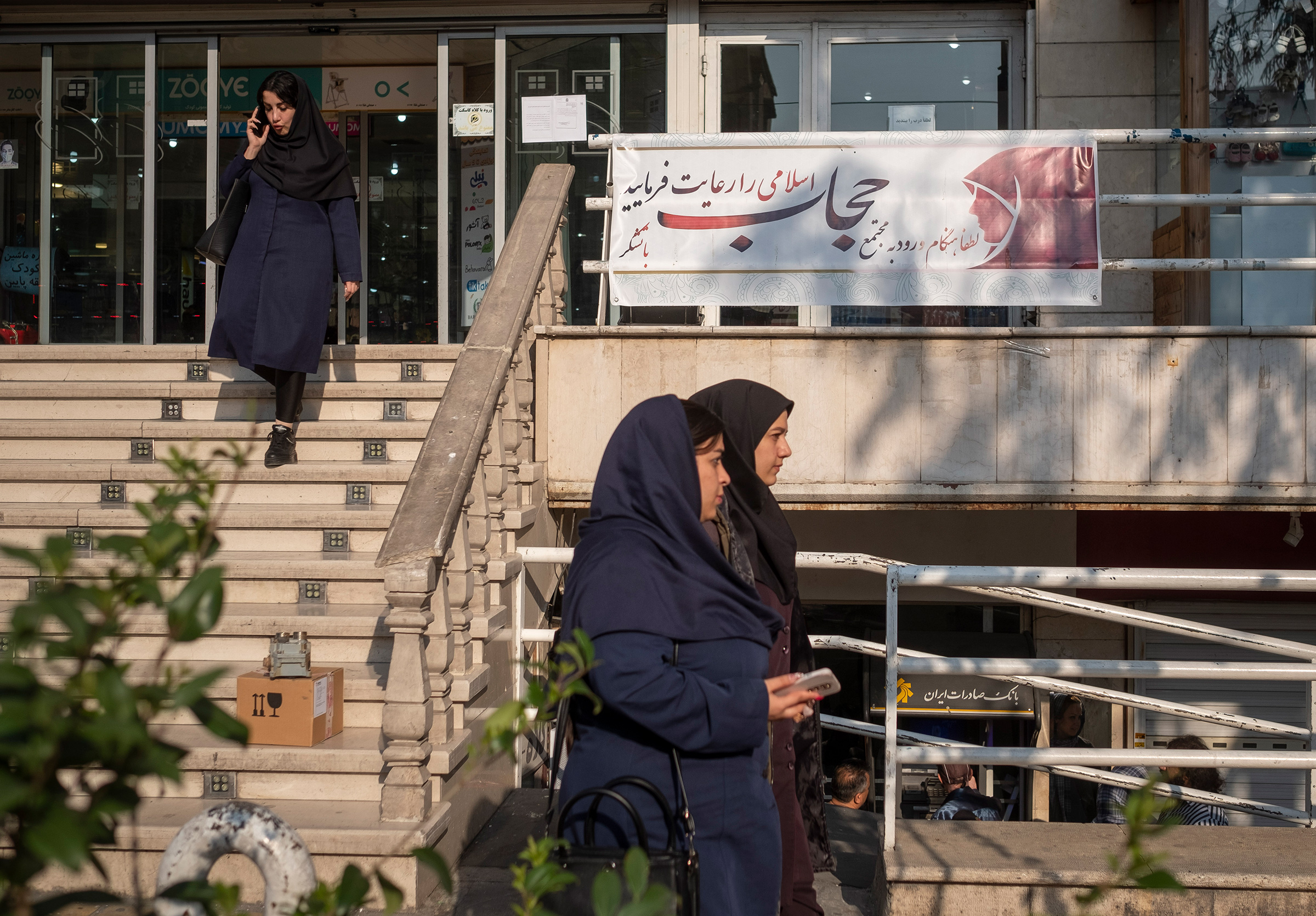 Iranian women walk past a sign reading, "Please observe Islamic hijab when entering the complex," in front of the main entrance of a shopping center in downtown Tehran on April 17. 