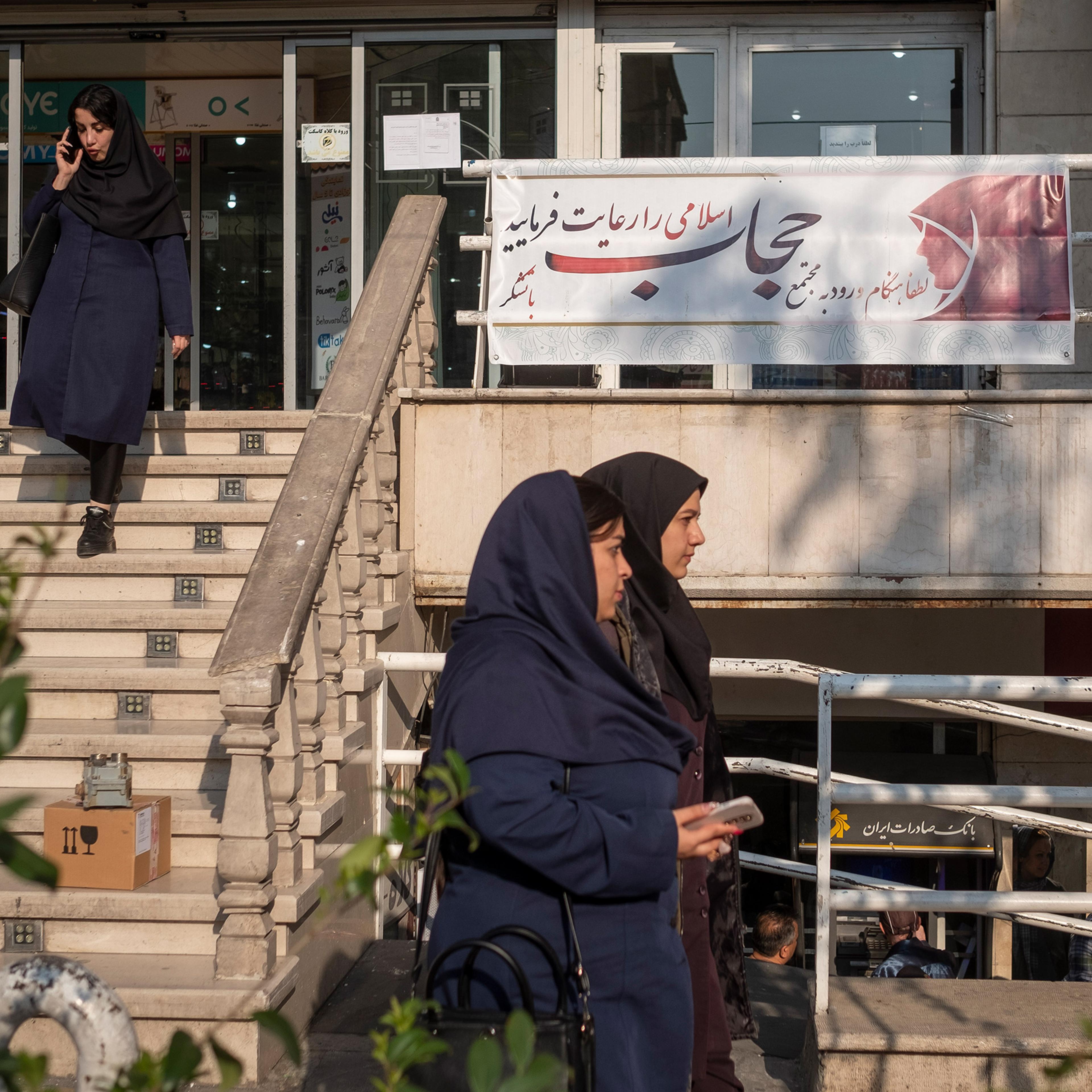 Iranian women walk past a sign reading, "Please observe Islamic hijab when entering the complex," in front of the main entrance of a shopping center in downtown Tehran on April 17.