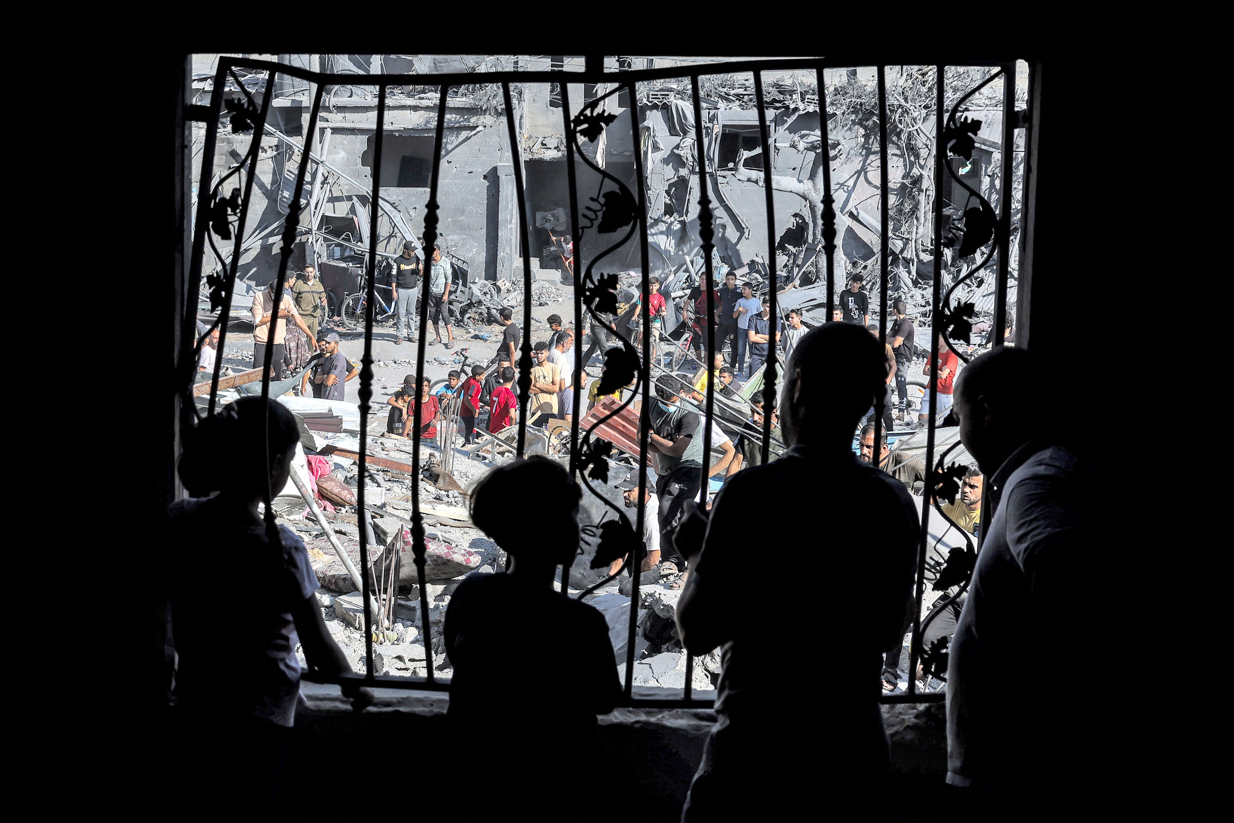 silhouettes of people stand behind the metal mesh that covered the window of a building that was hit by Israeli bombardment in Rafah in the southern Gaza Strip
