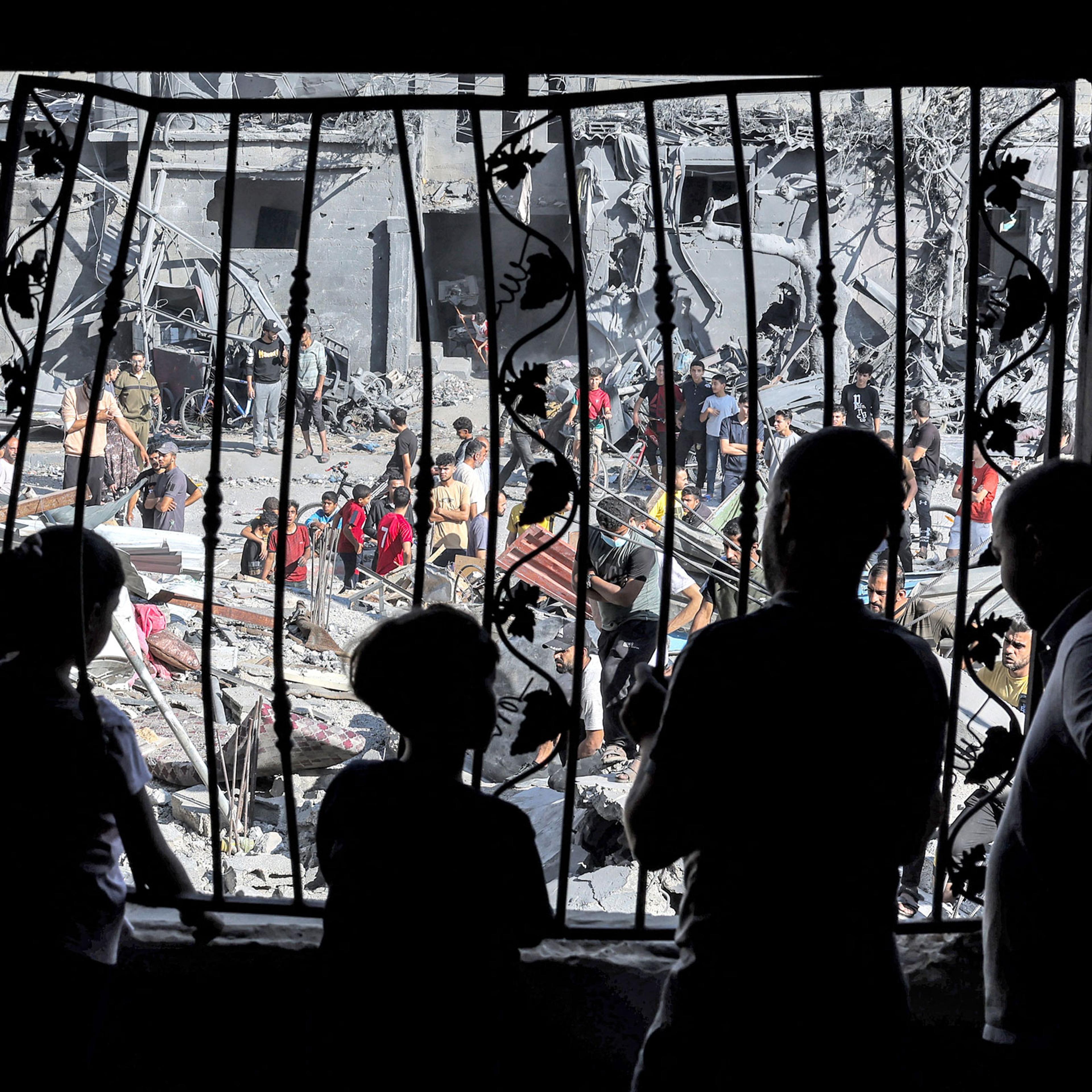 silhouettes of people stand behind the metal mesh that covered the window of a building that was hit by Israeli bombardment in Rafah in the southern Gaza Strip