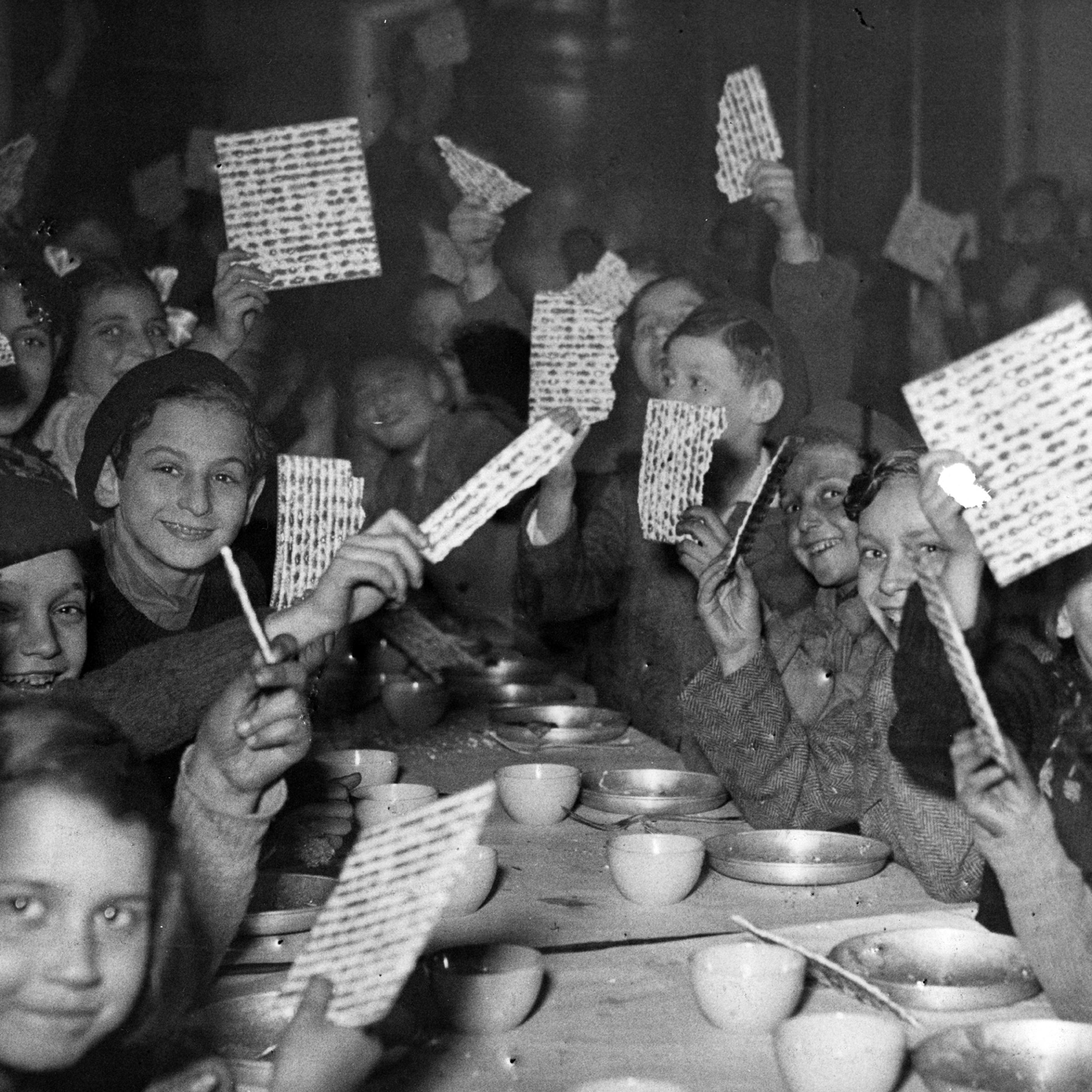 Young refugees at a Passover Seder holding up their matzot with pride at a children's canteen run by the JDC partner Federation des Societes Juives en France. France, c. 1947. Photographer unknown.