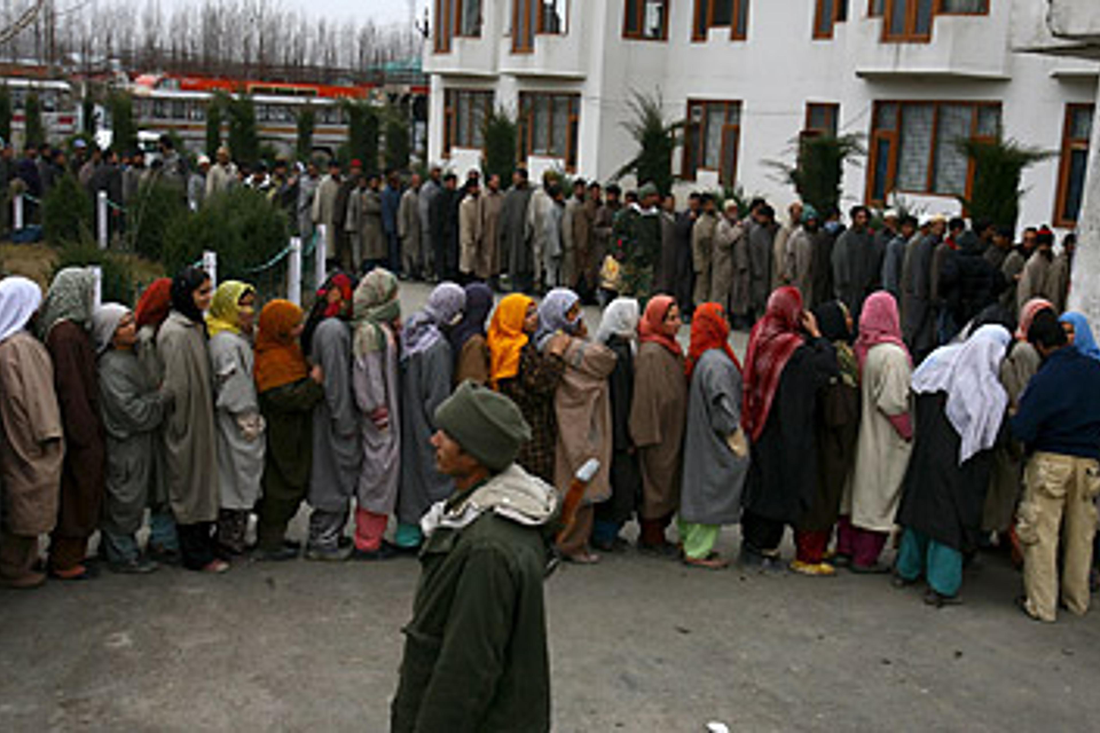 An Indian paramilitary soldier stands guard as Kashmiri Muslims stand in a queue to cast their votes outside a polling station in Srinagar, the summer capital of Indian Kashmir, 24, December, 2008.