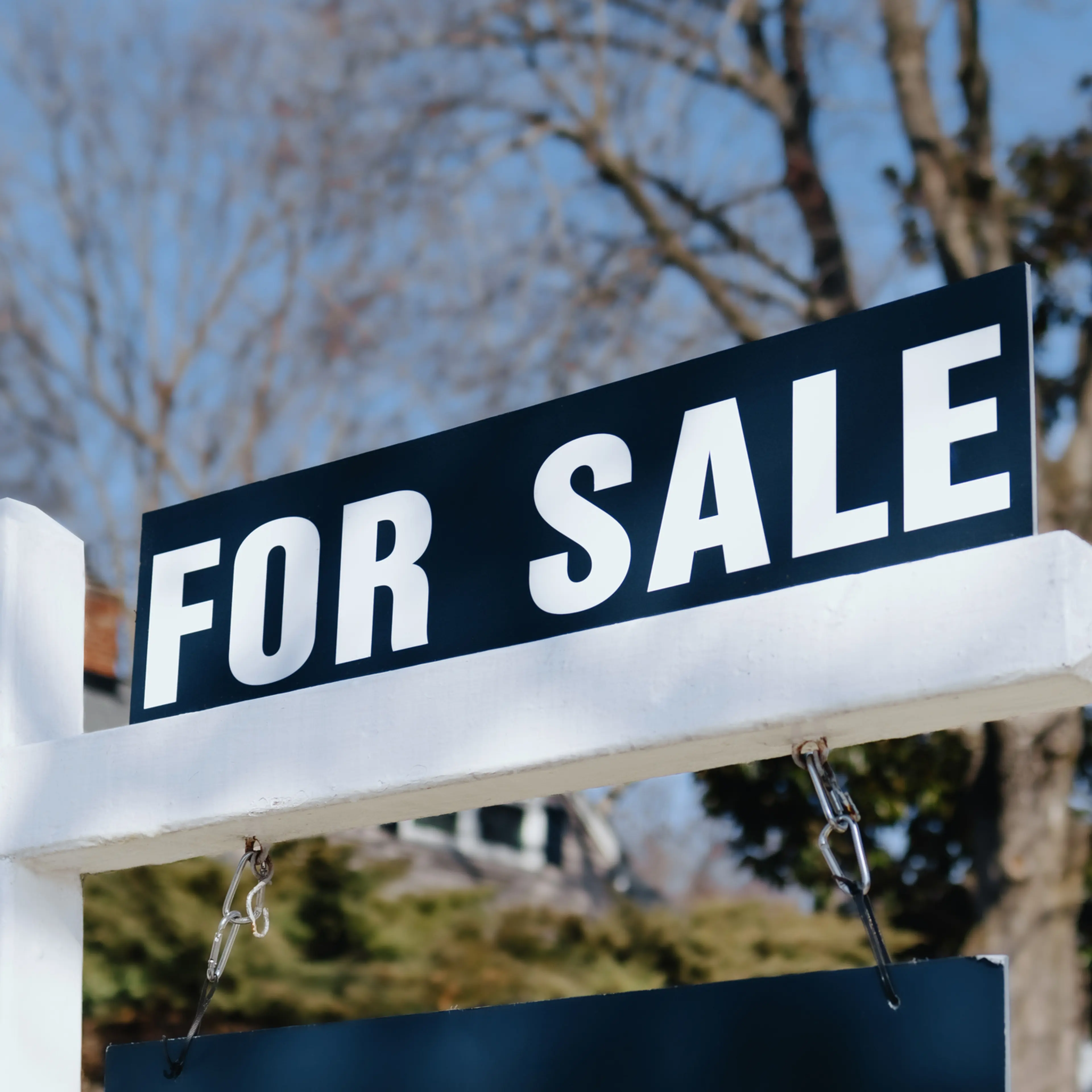 For Sale Sign Hangs in Front Yard of House