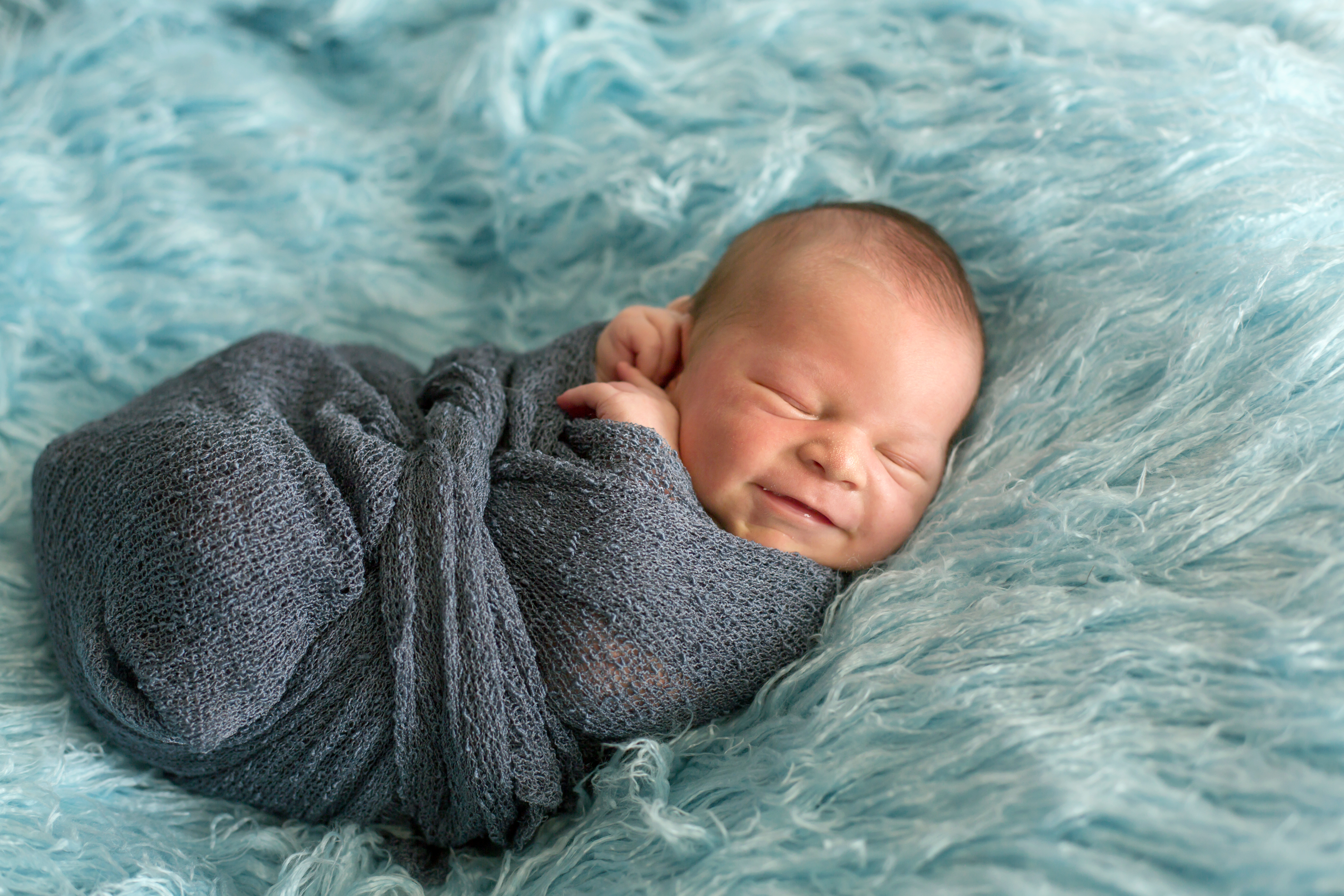 Happy smiling newborn baby in wrap, sleeping happily in cozy blue fur, cute infant baby