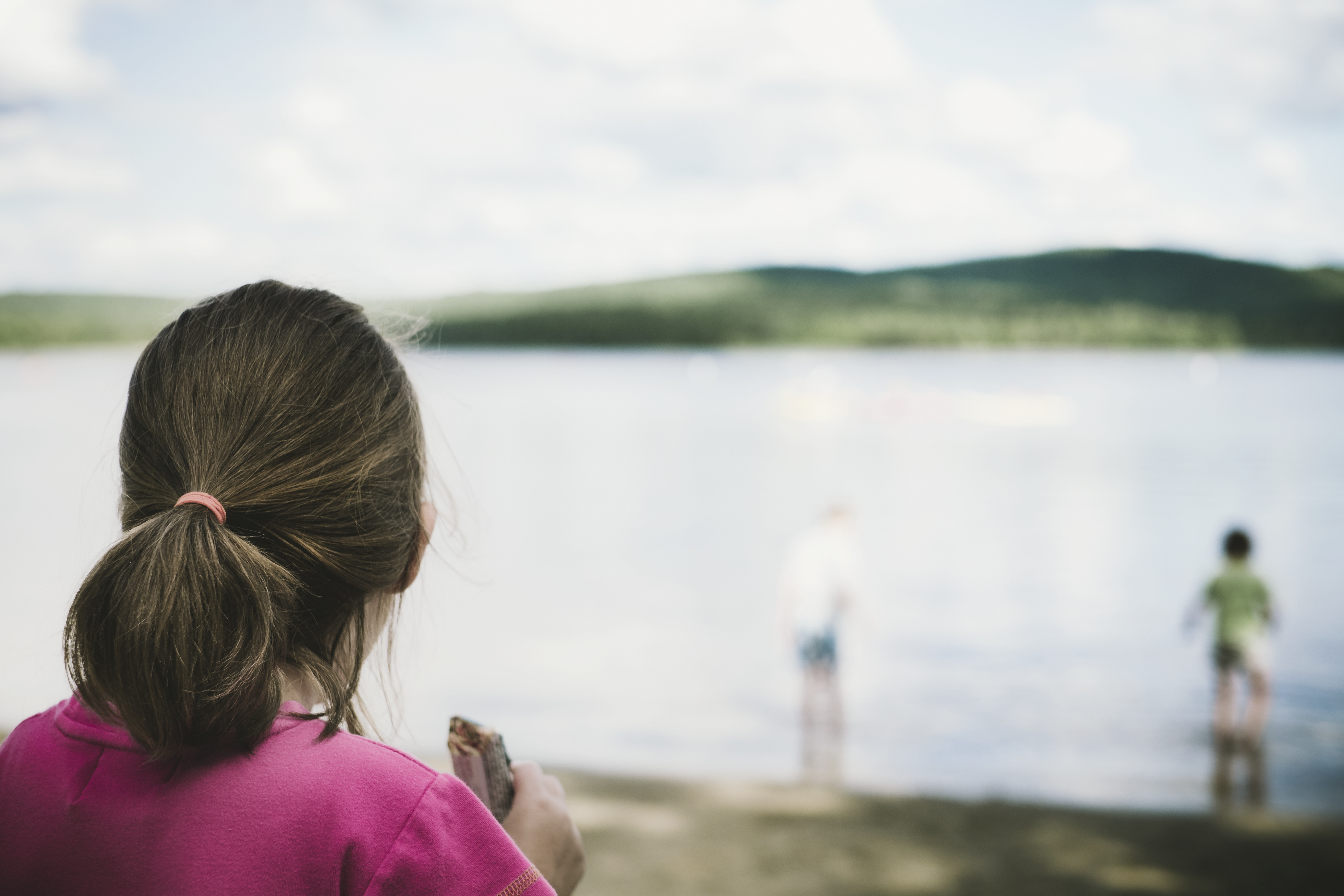 Girl With Ponytail Eating A Granola Bar And Gazing At A Lake