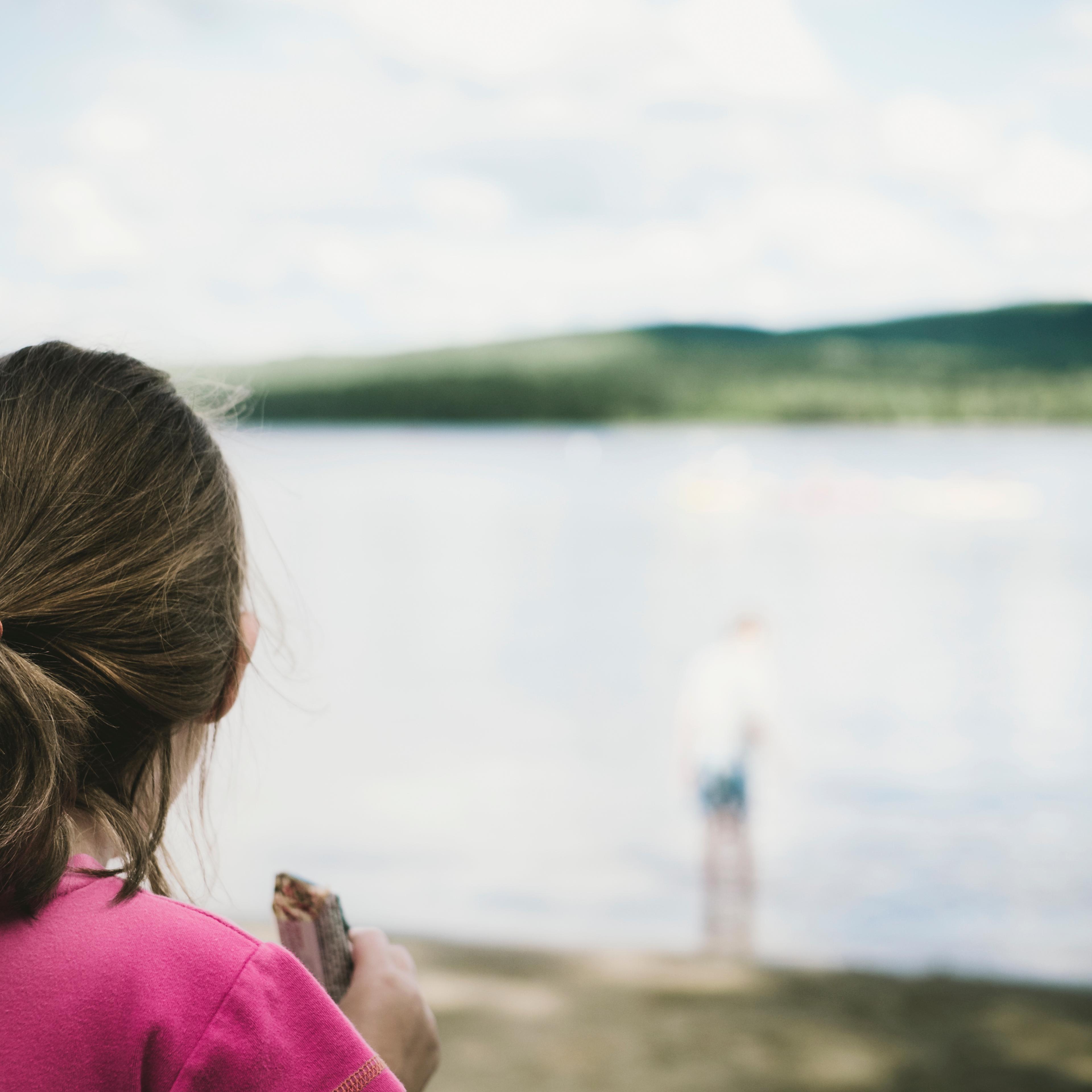Girl With Ponytail Eating A Granola Bar And Gazing At A Lake