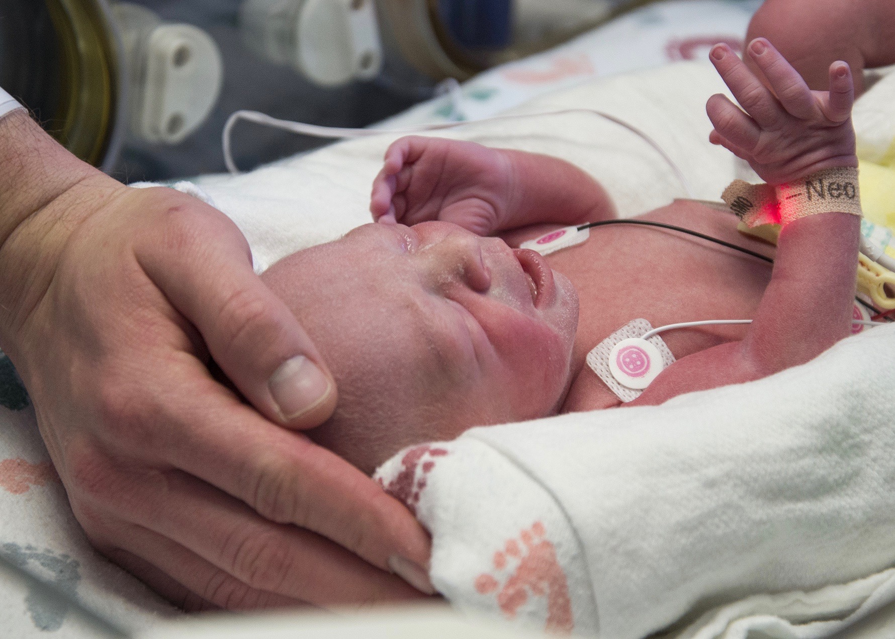The baby's father rests his hand on the child.