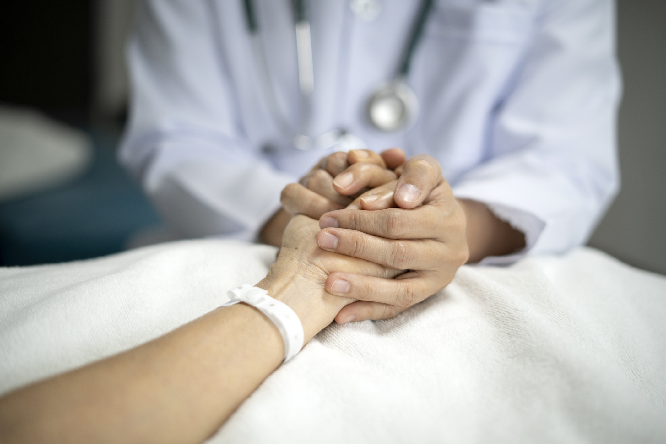 Midsection Of Doctor holding hand of senior woman patient giving support and love to her on bed at the hospital.