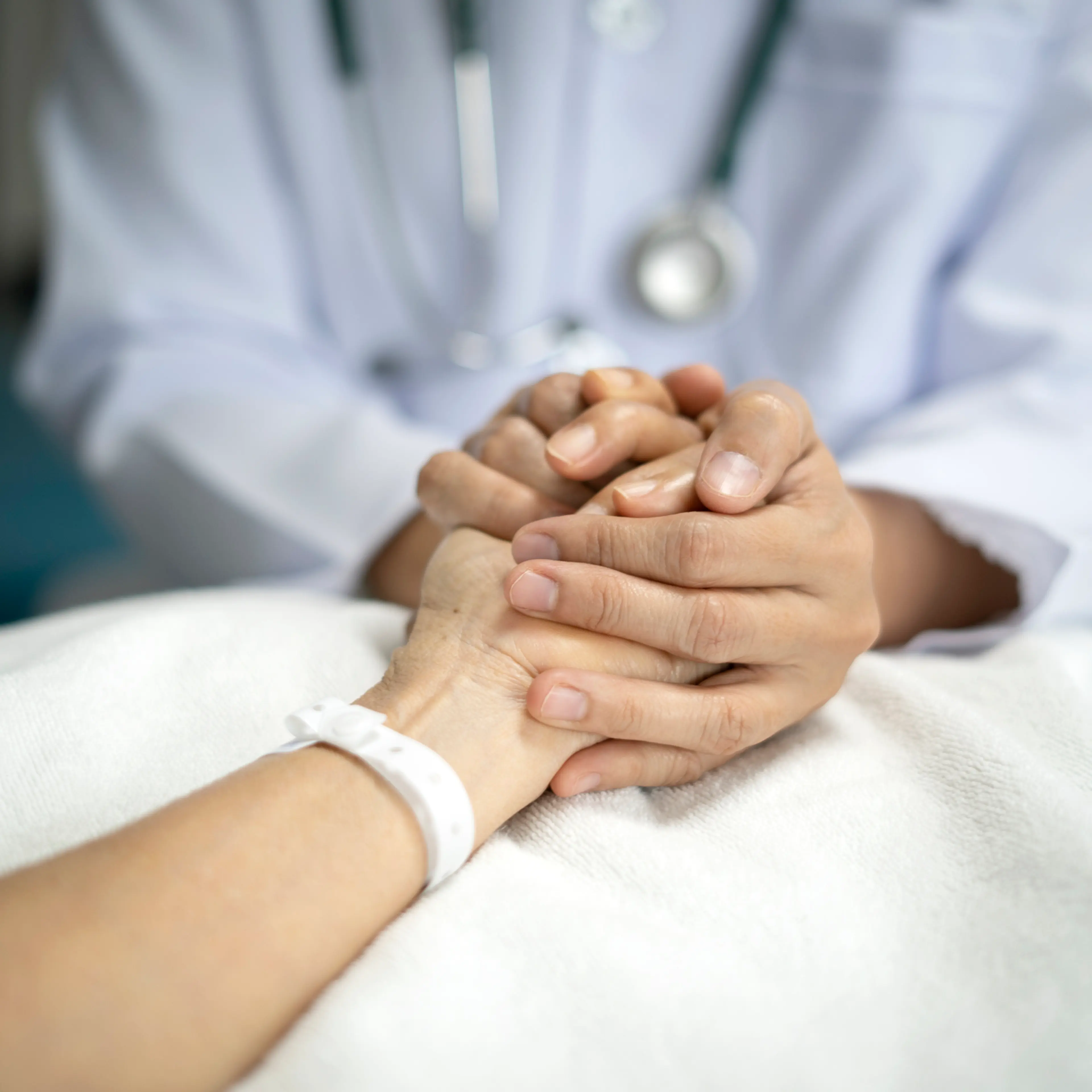Midsection Of Doctor holding hand of senior woman patient giving support and love to her on bed at the hospital.